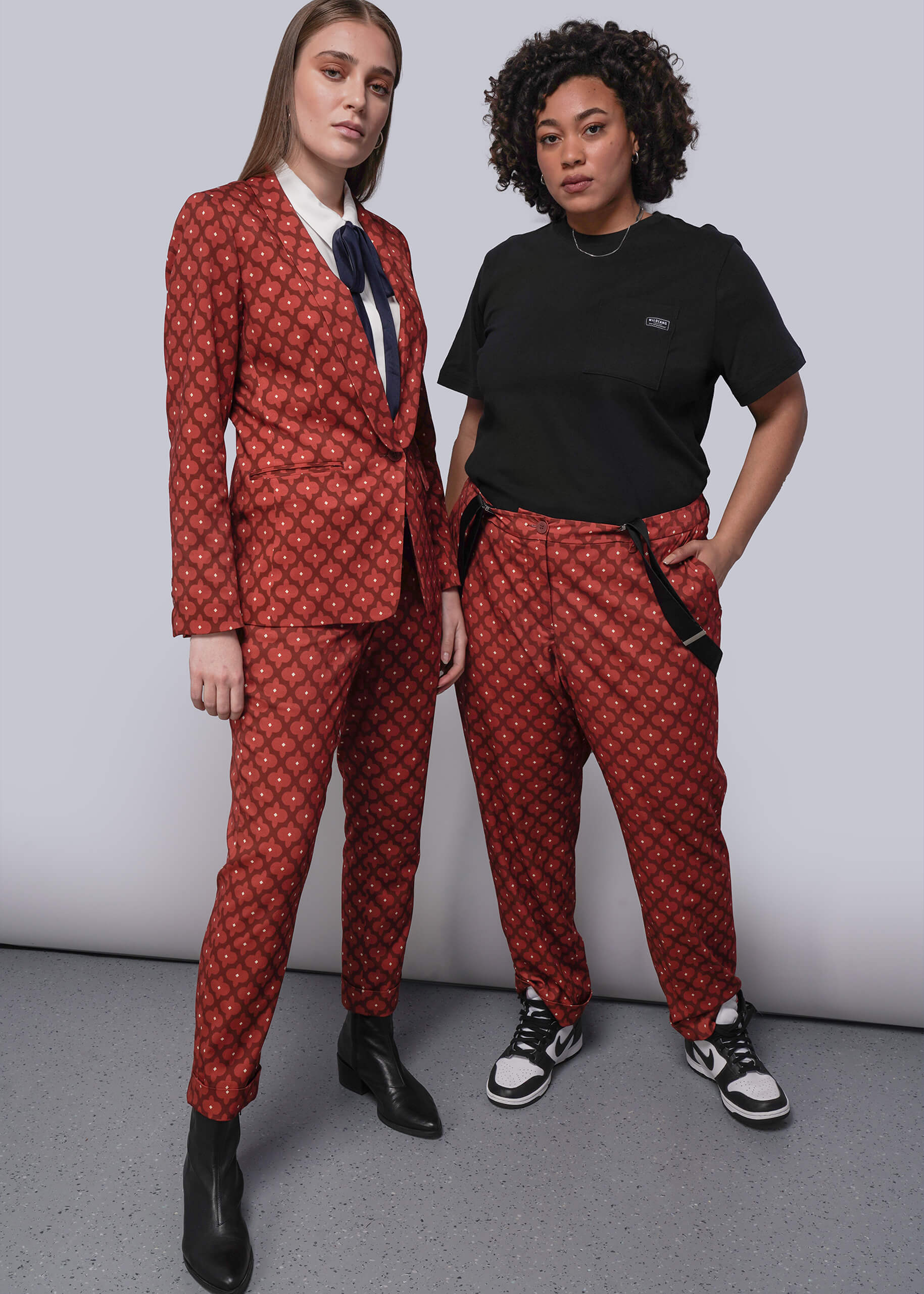 Two people wearing matching red patterned suits against a plain background