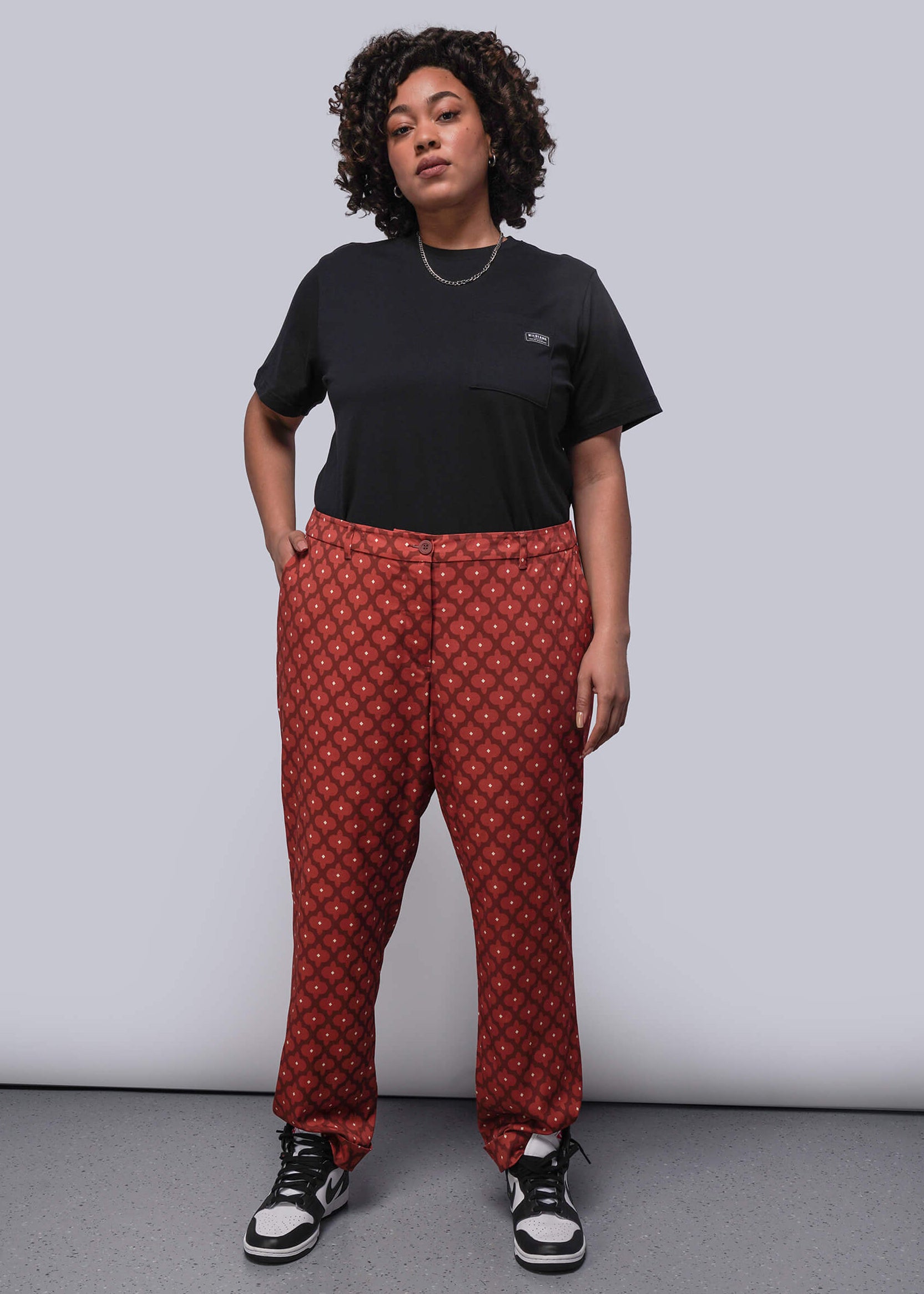 1X=Person wearing a black t-shirt and red patterned pants against a plain background