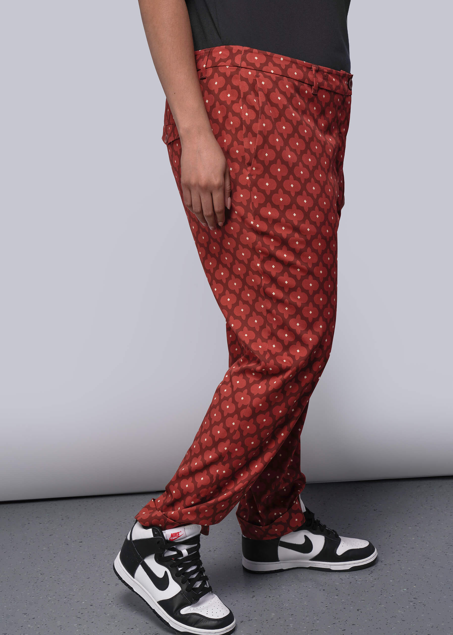 1X=Person wearing red patterned pants and black and white sneakers on a gray background