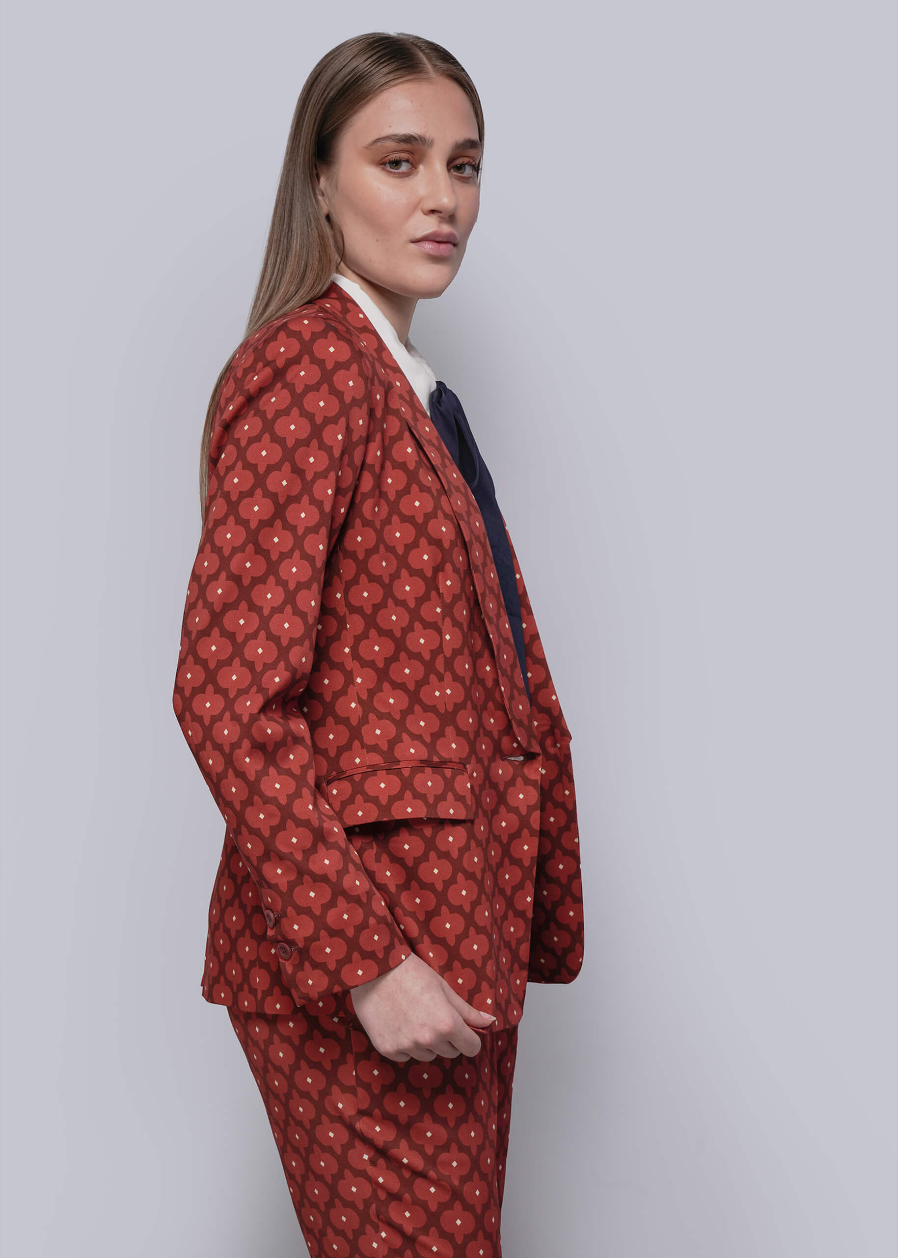 S=Woman wearing a red patterned suit against a plain background