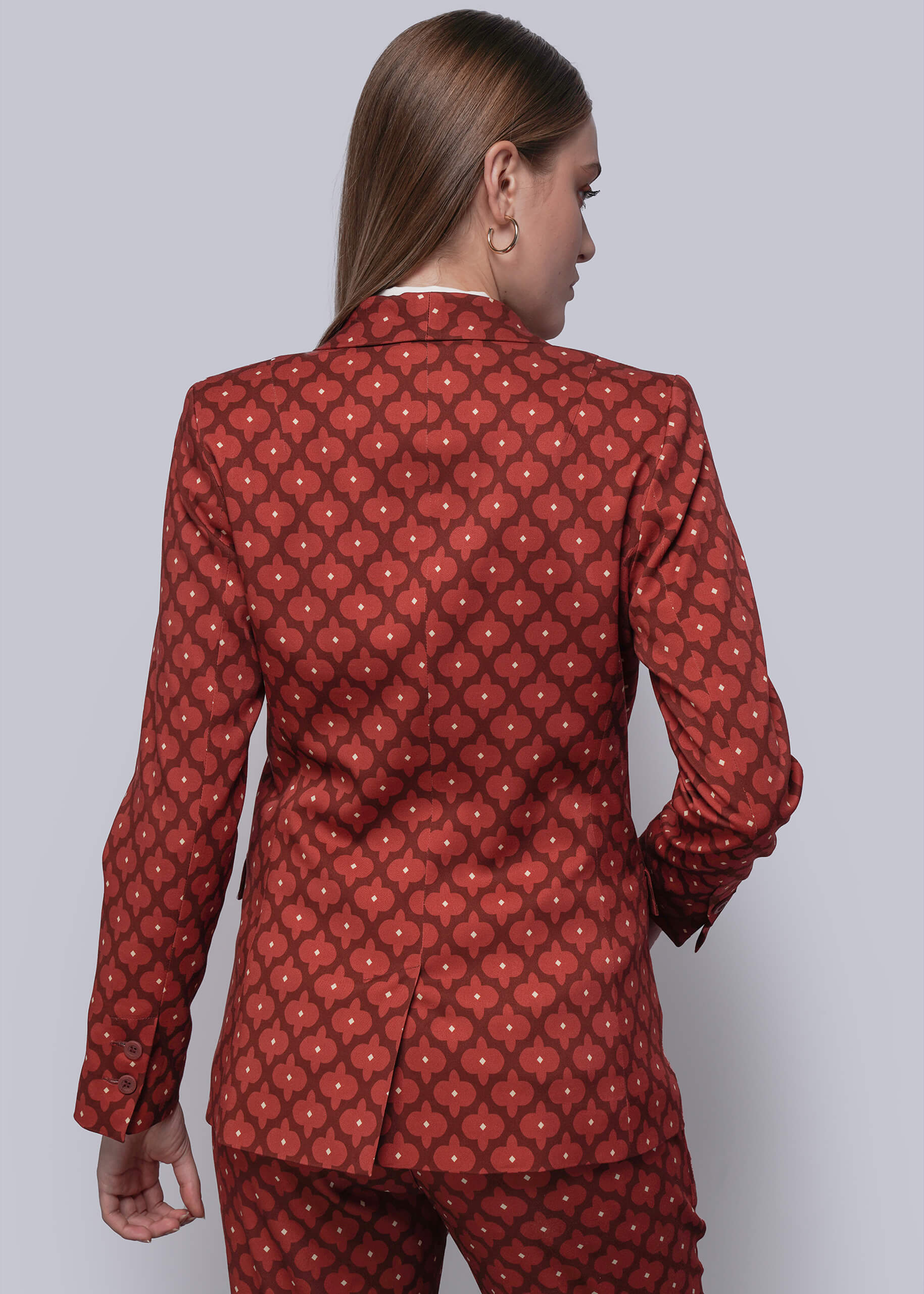 S=Woman wearing a red patterned blazer and pants on a plain background