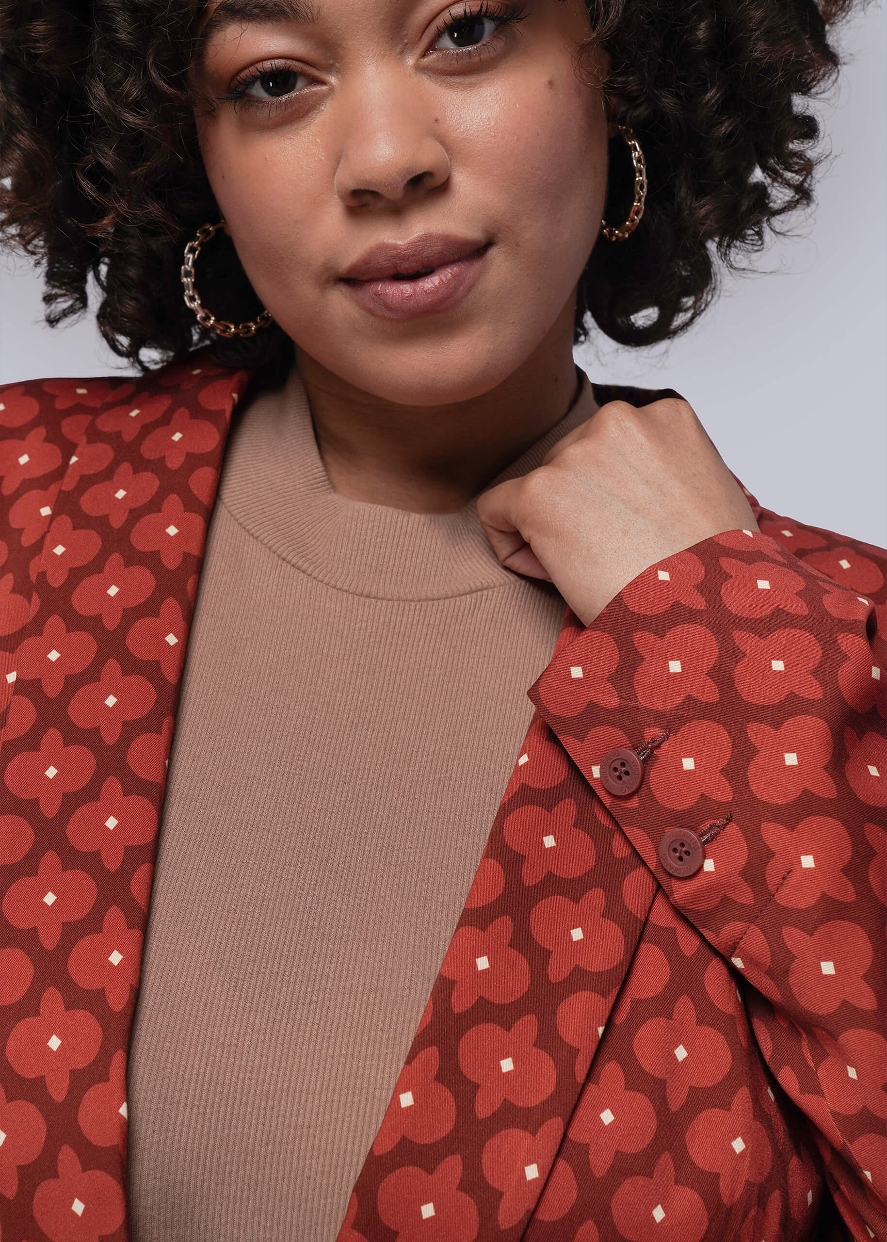 1X=Person wearing a red patterned blazer over a brown top against a neutral background