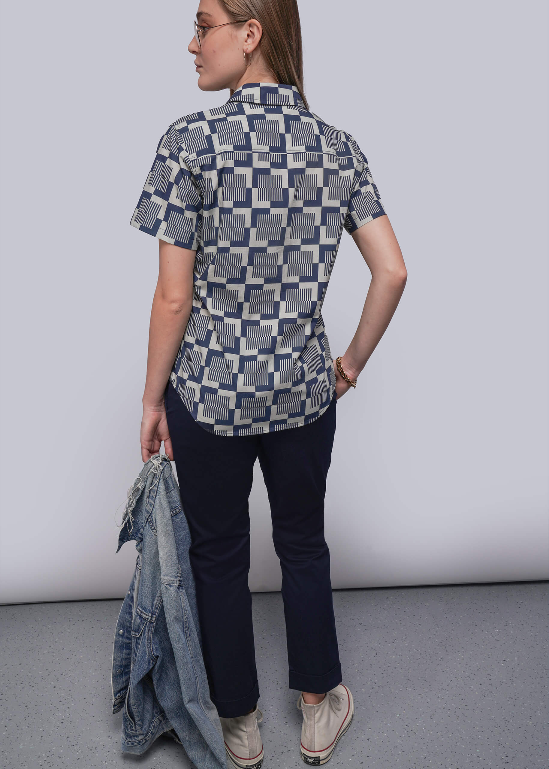 S=Person wearing a patterned shirt and dark pants against a plain background