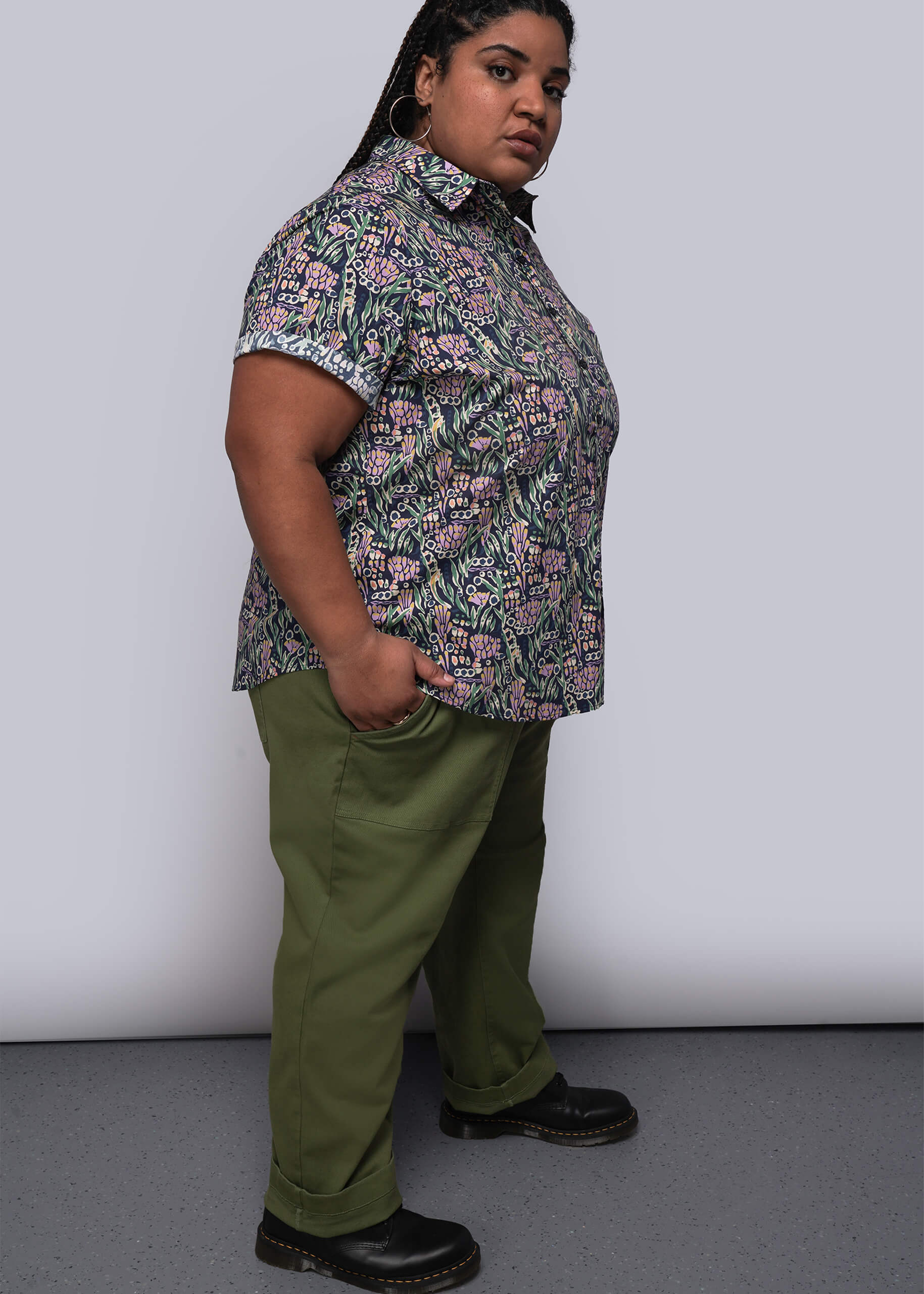 1X=Person wearing a patterned shirt and green pants against a plain background