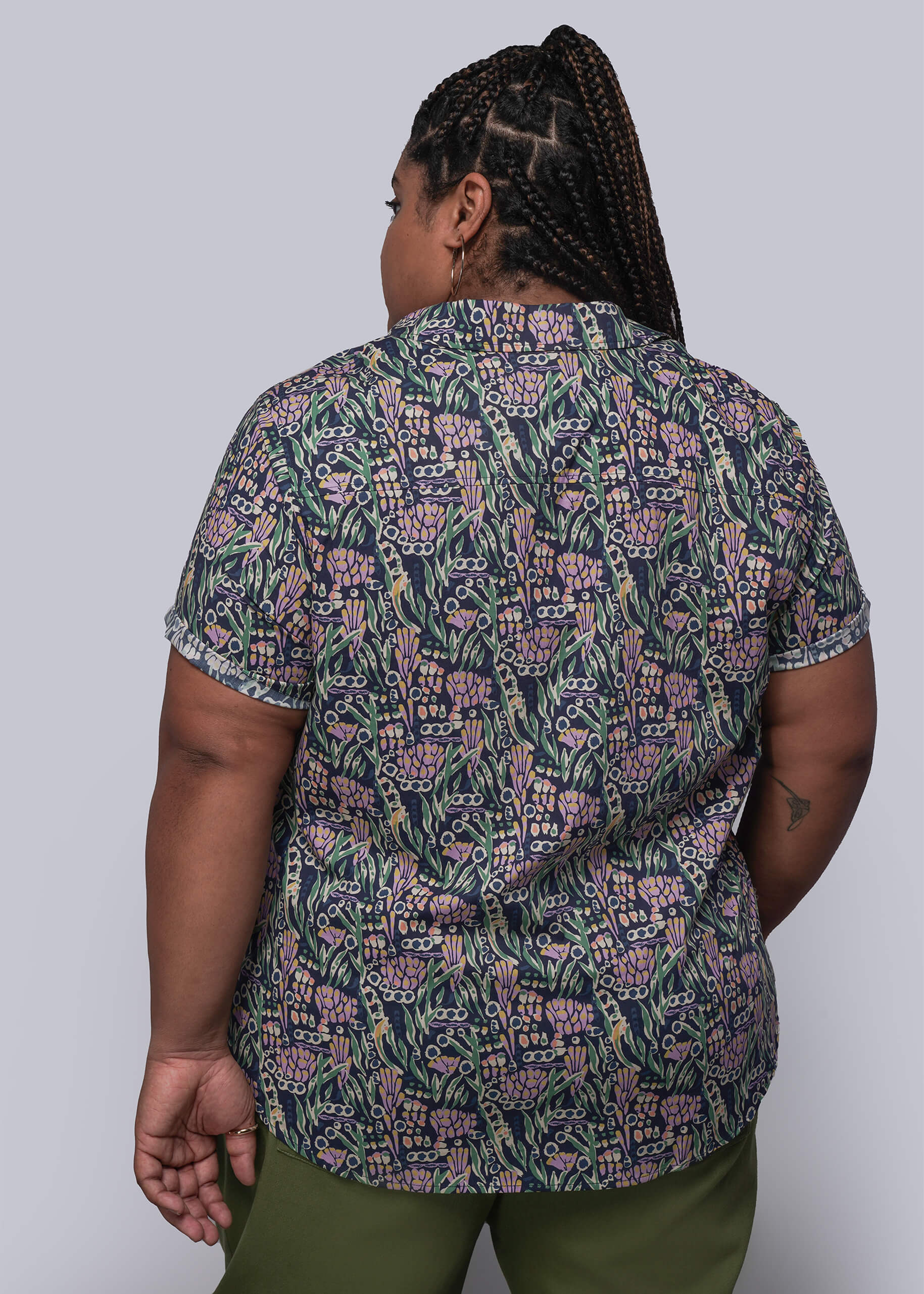 1X=Person wearing a patterned shirt and green pants against a plain background