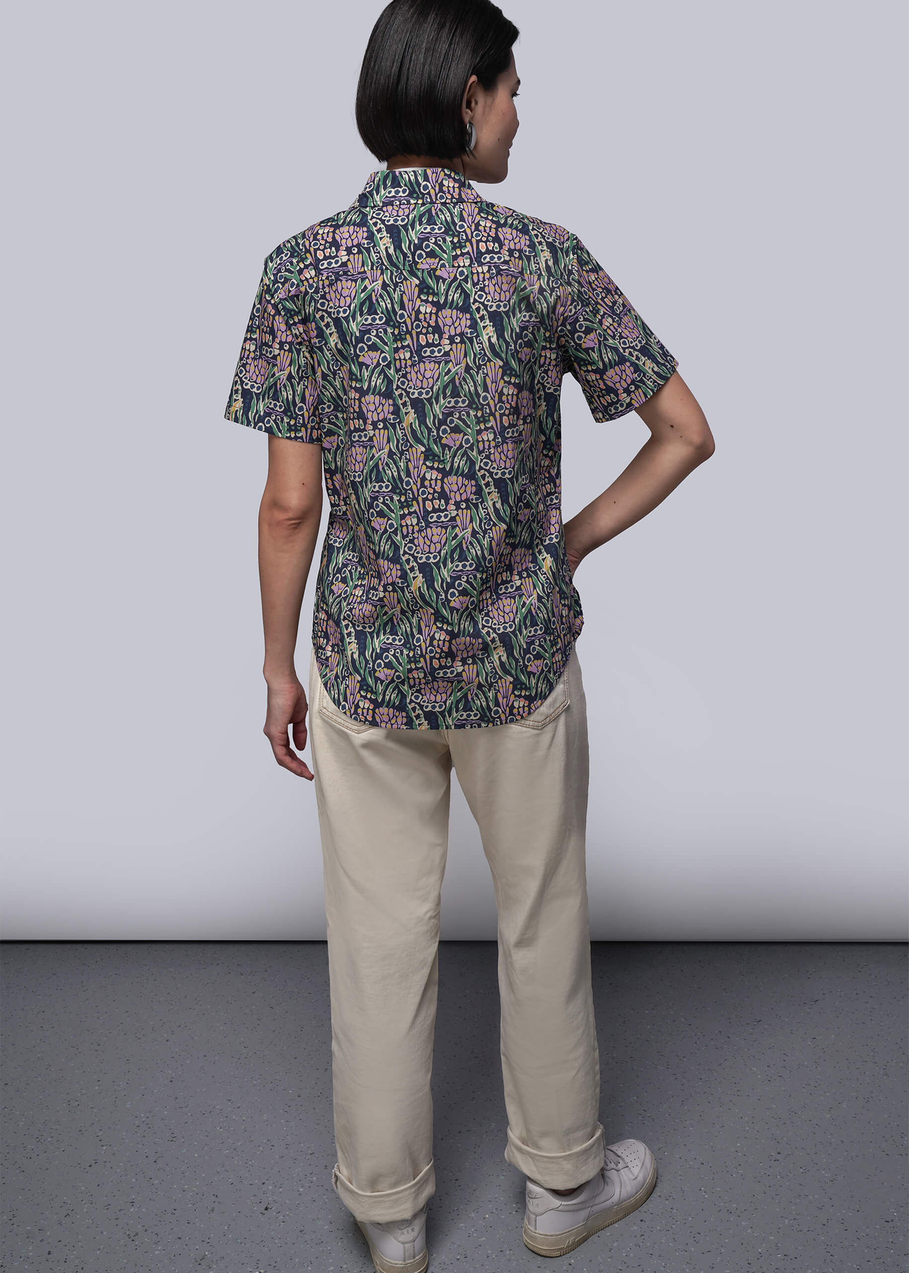 S=Person wearing a patterned shirt and beige pants against a plain background