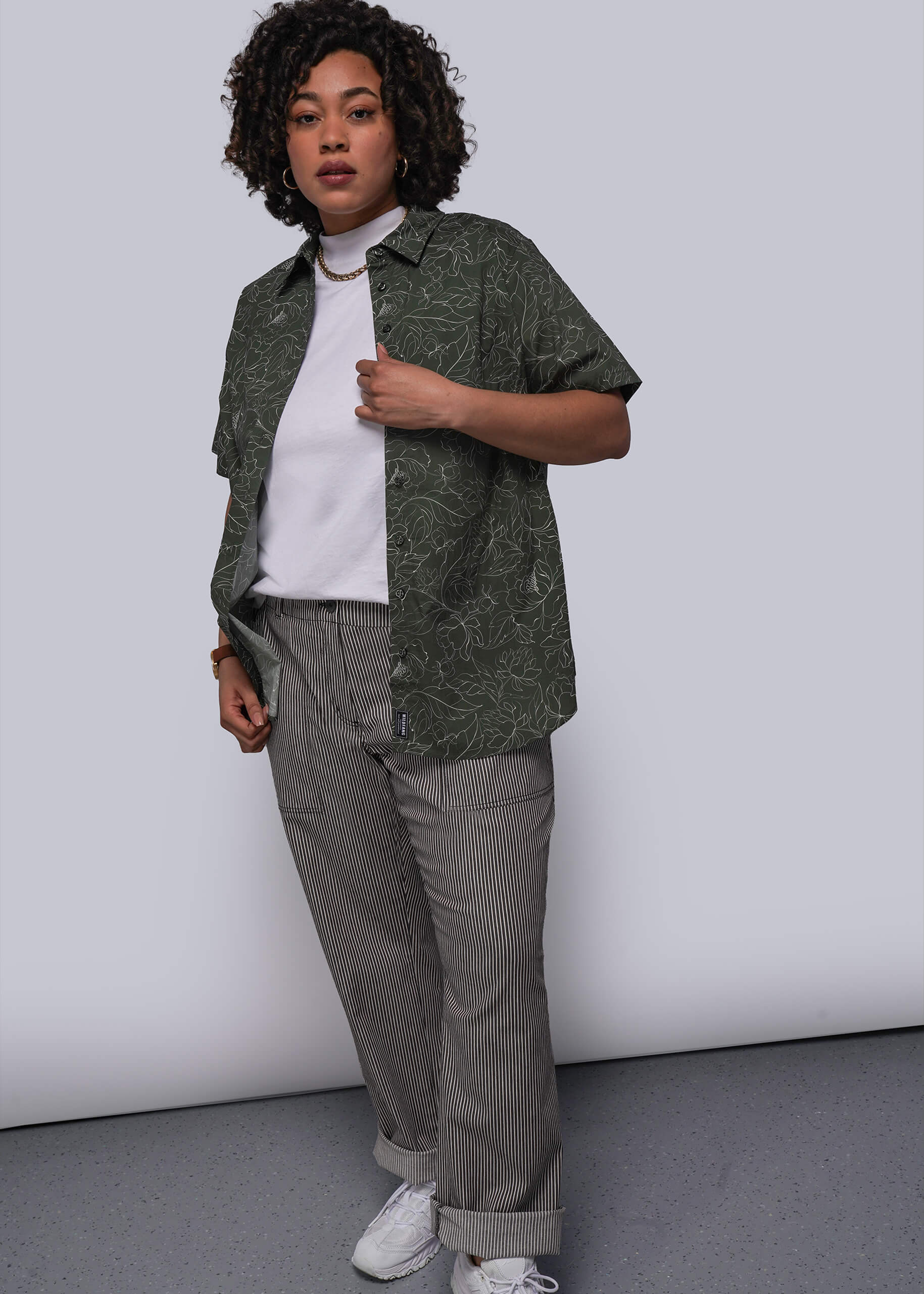 1X=Person wearing a green patterned shirt, white t-shirt, gray pants, and white sneakers against a plain background