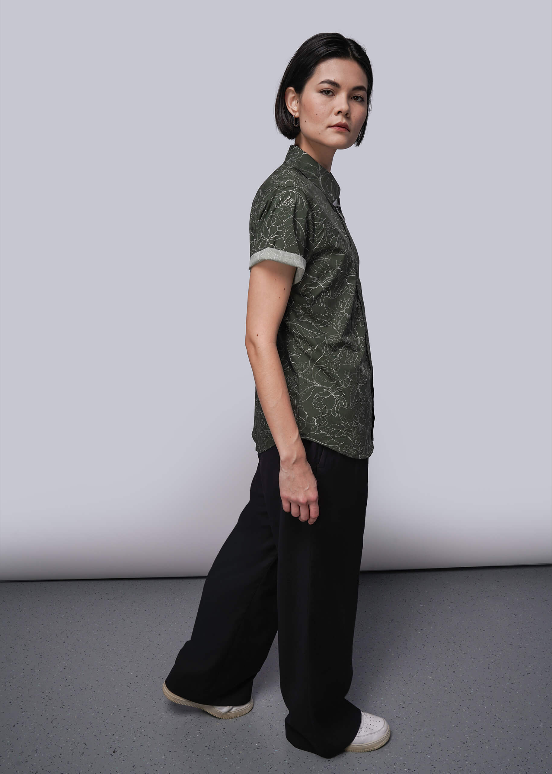 S=Person wearing a green patterned shirt and black pants against a white background