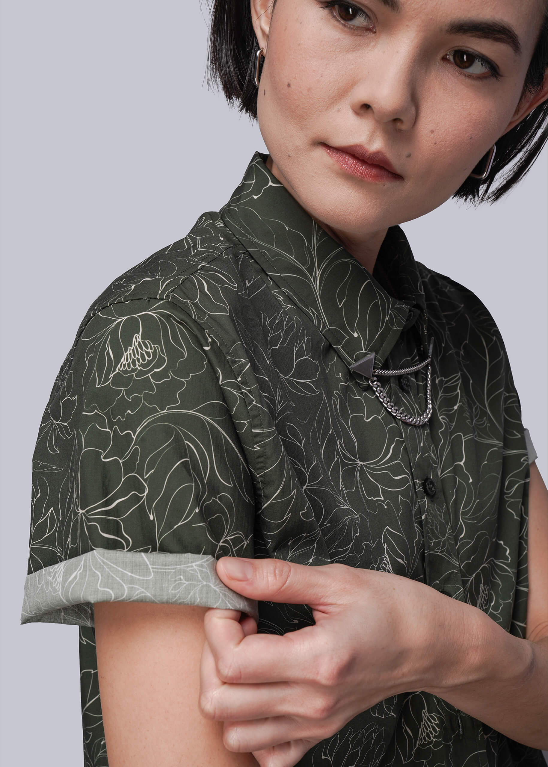 S=Person wearing a dark green patterned shirt against a light gray background