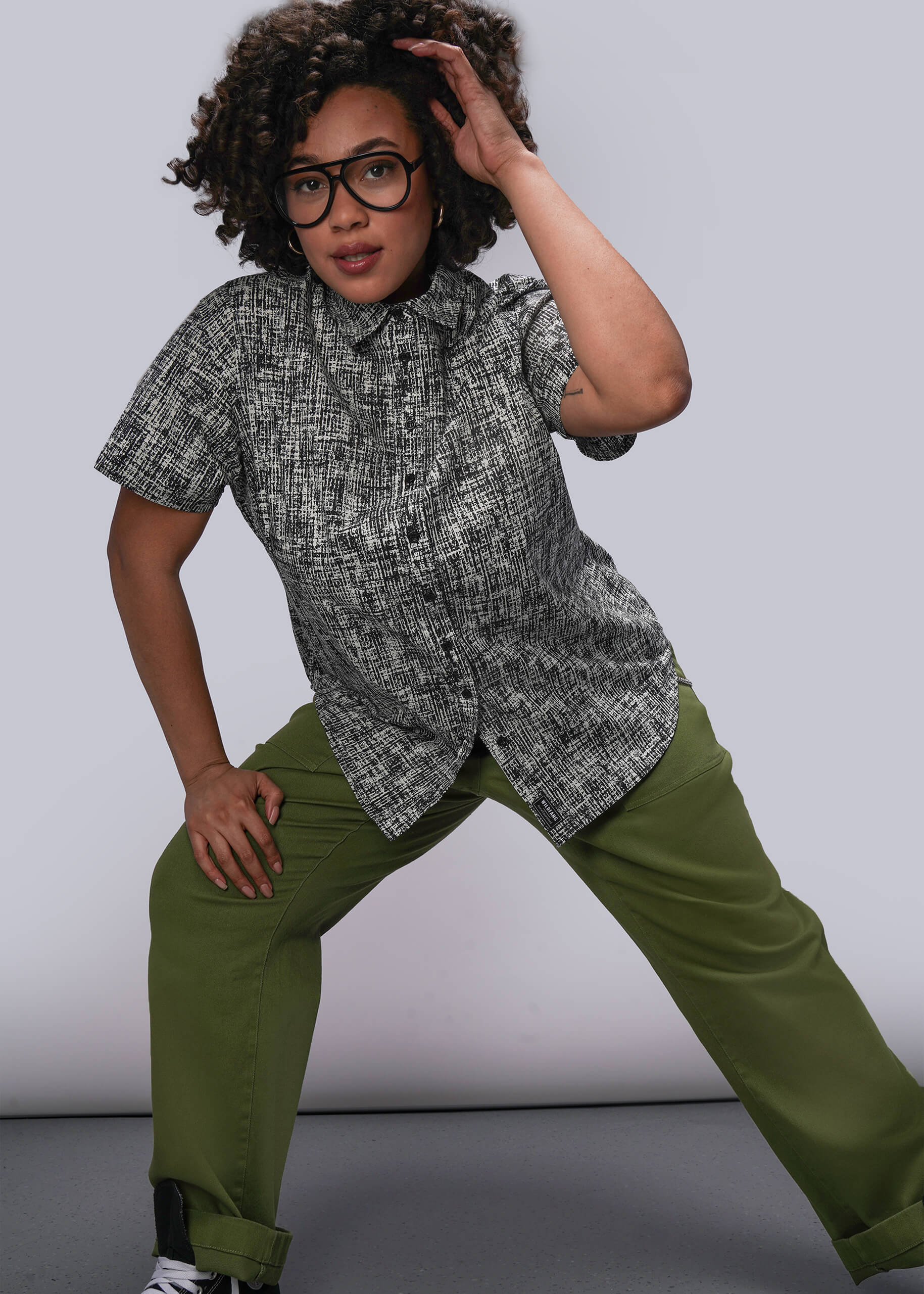 1X=Person wearing a patterned shirt and green pants against a plain background