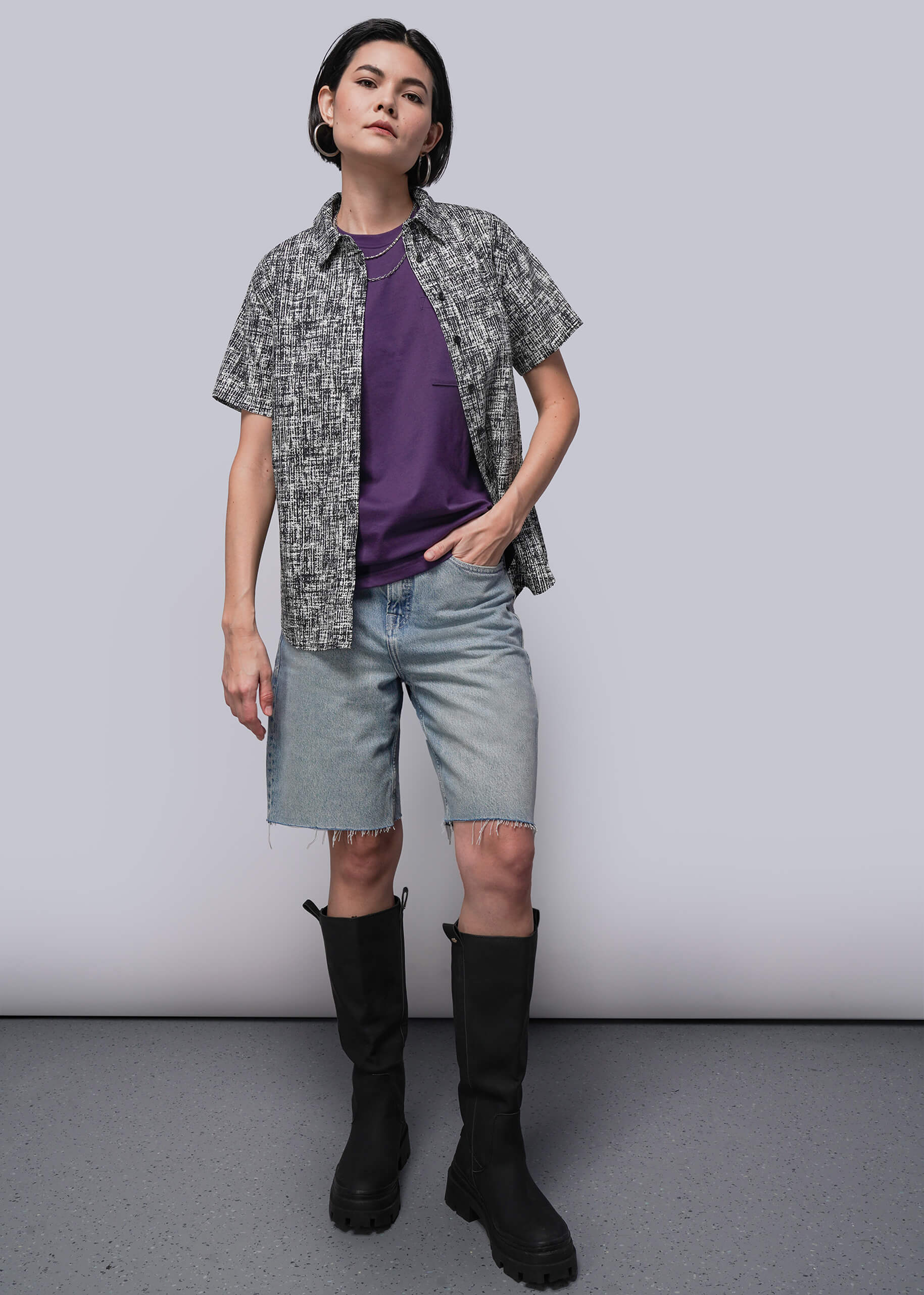 S=Person wearing a patterned shirt, purple top, denim shorts, and black boots on a plain background