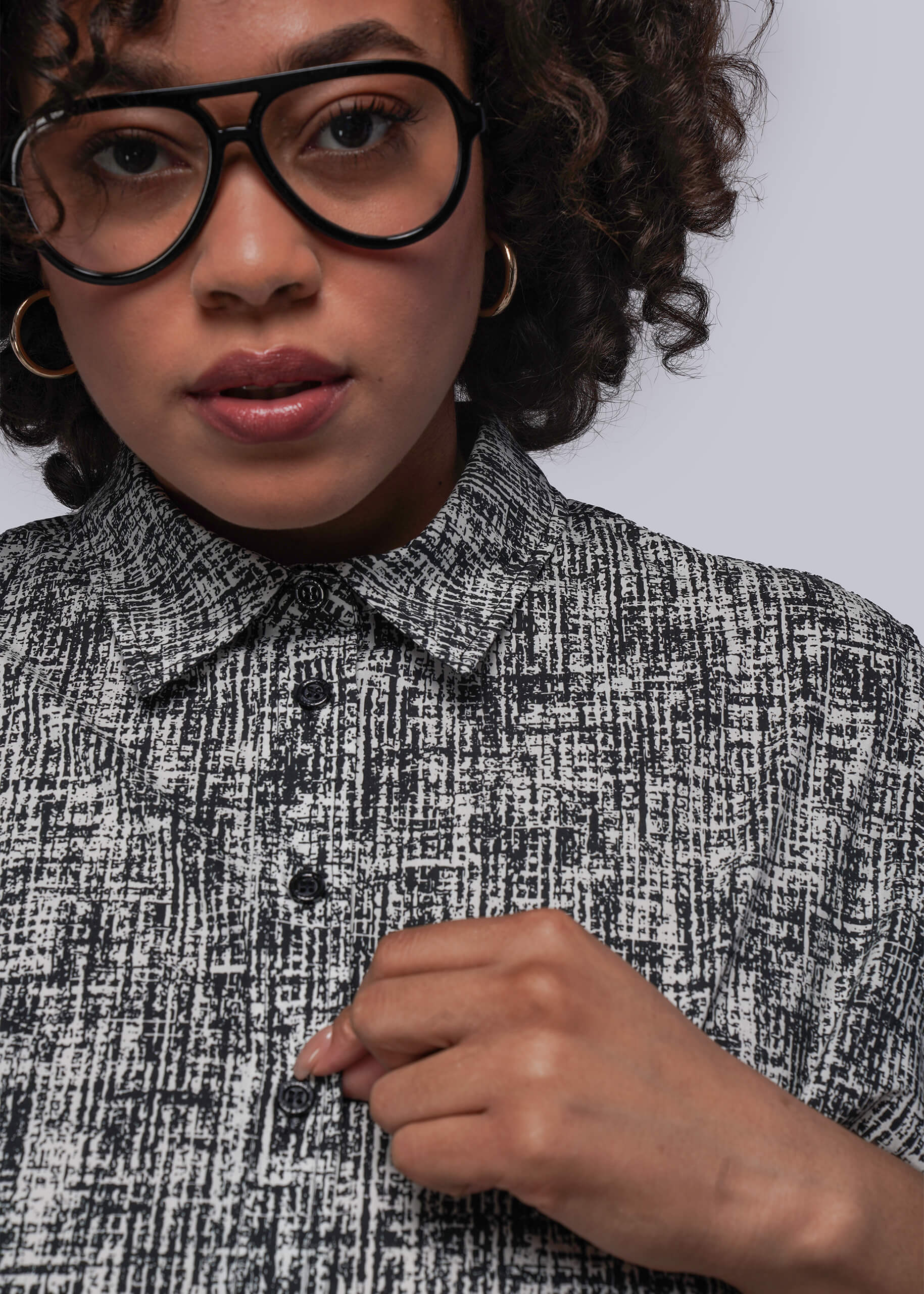 1X=Person wearing a black and white patterned shirt with glasses and a neutral background