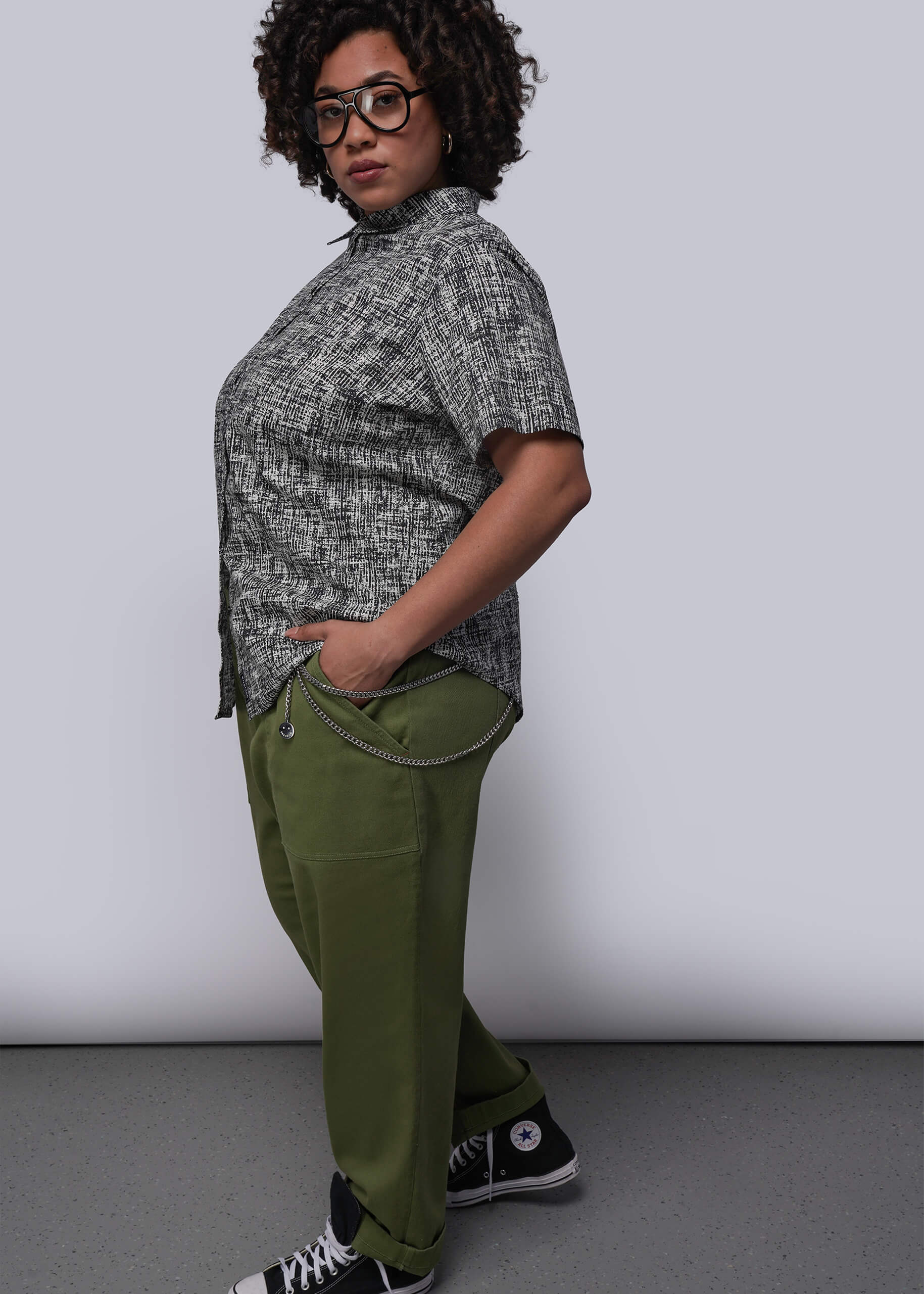 1X=Person wearing a patterned shirt and green pants against a plain background
