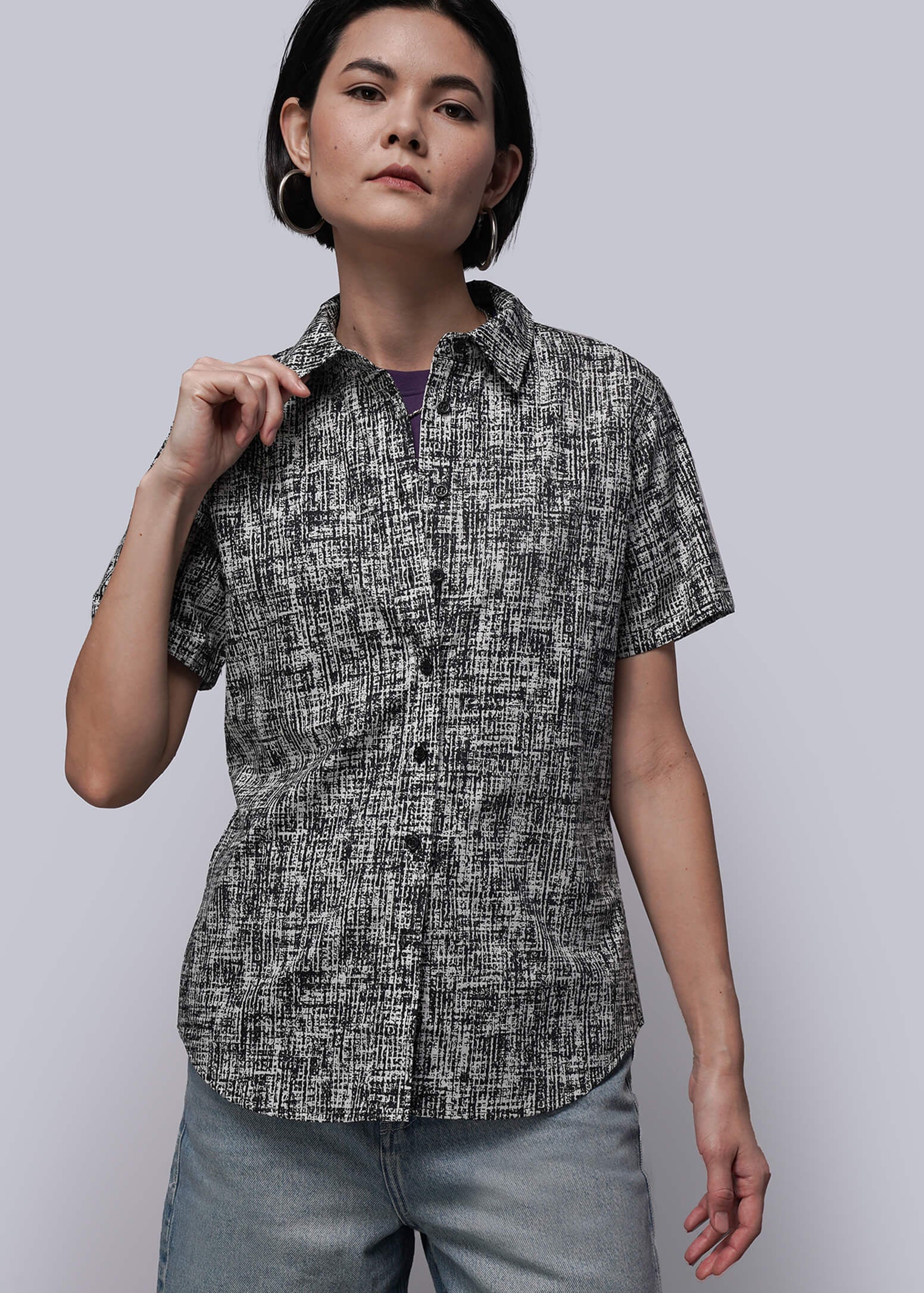 Woman wearing a patterned shirt and light blue pants against a plain background