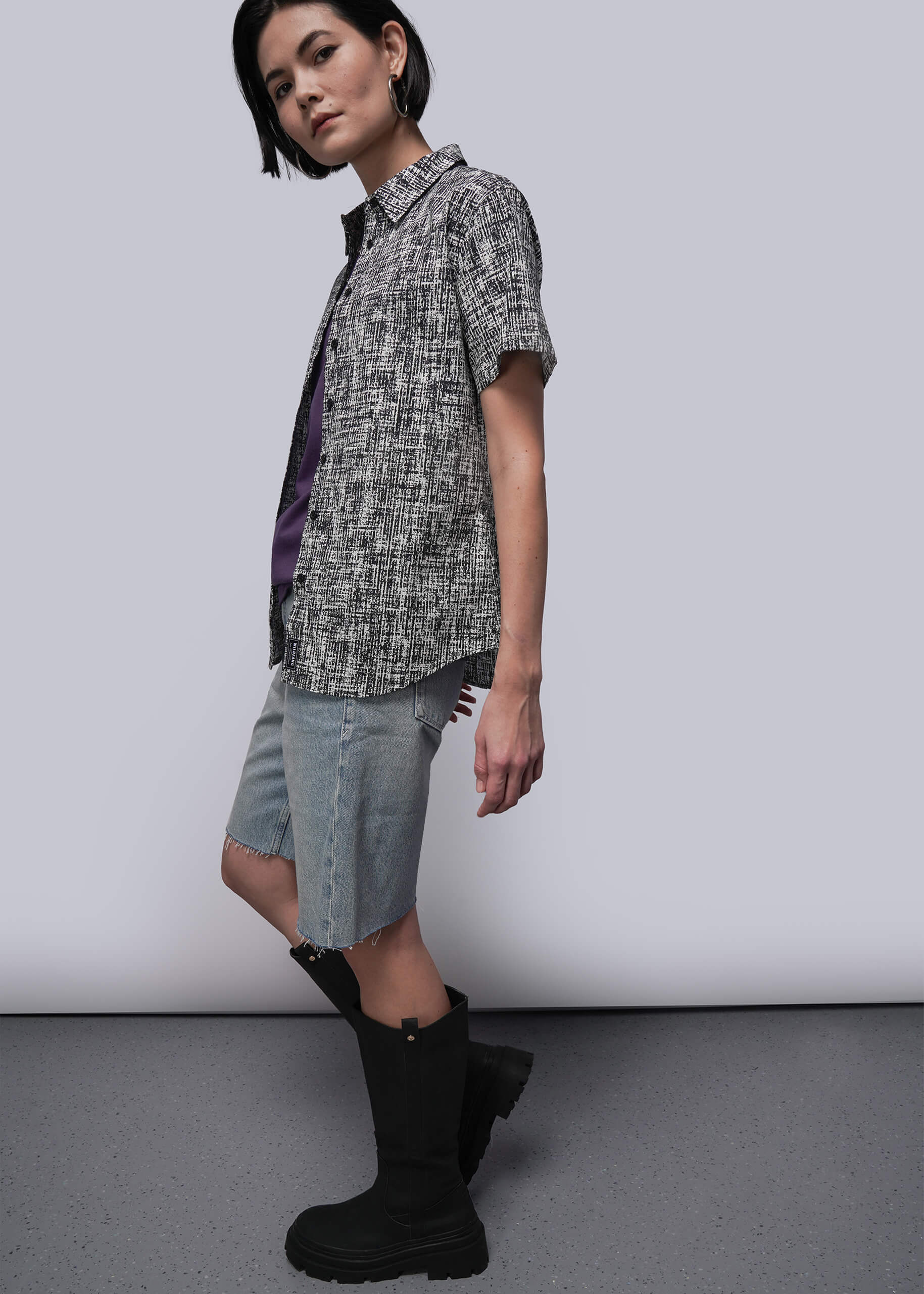 S=Person wearing a patterned shirt, denim shorts, and black boots against a plain background