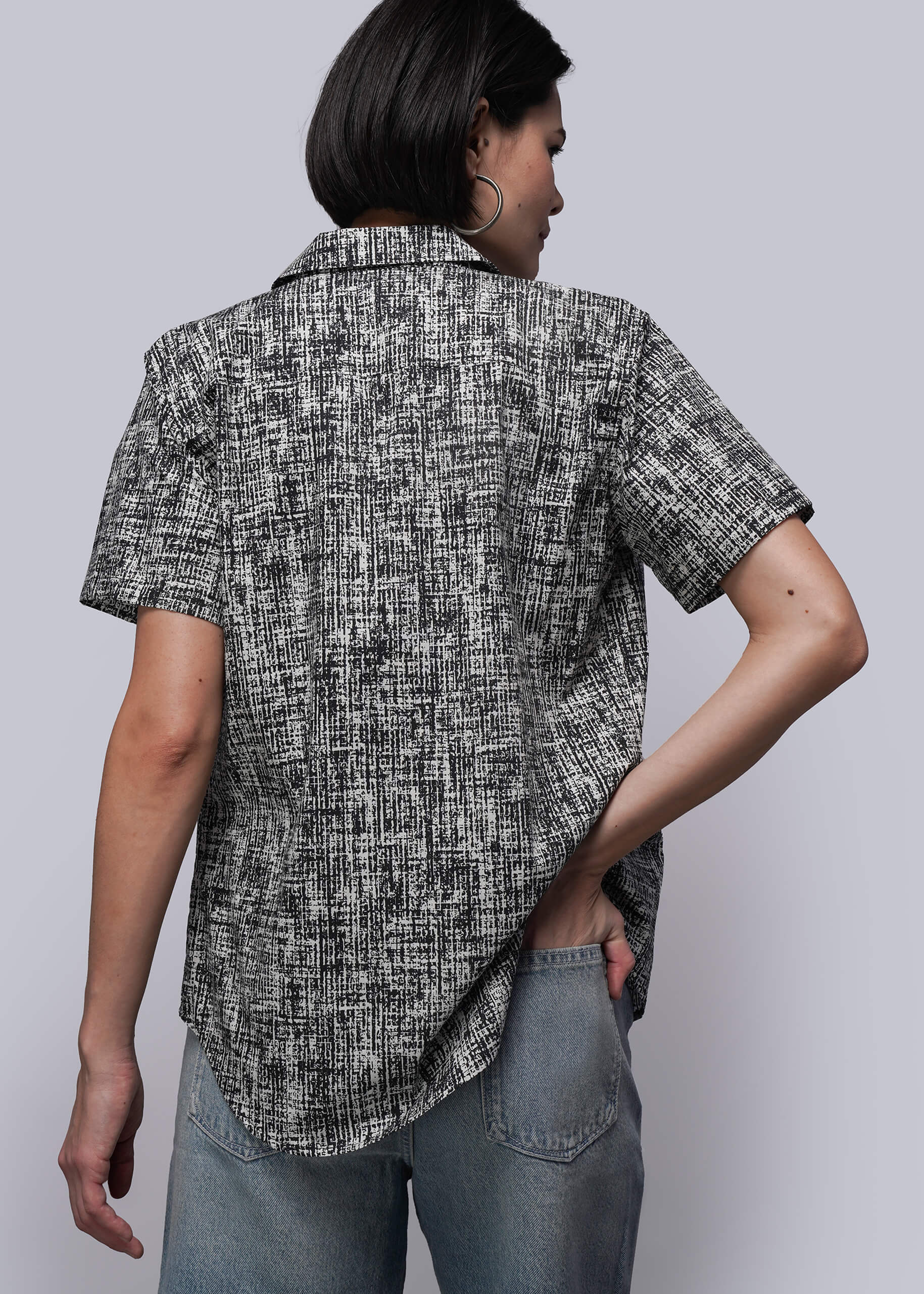 S=Person wearing a black and white patterned shirt with short sleeves on a plain background