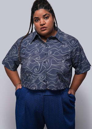 1X=Person wearing a patterned blue shirt and blue pants against a gray background