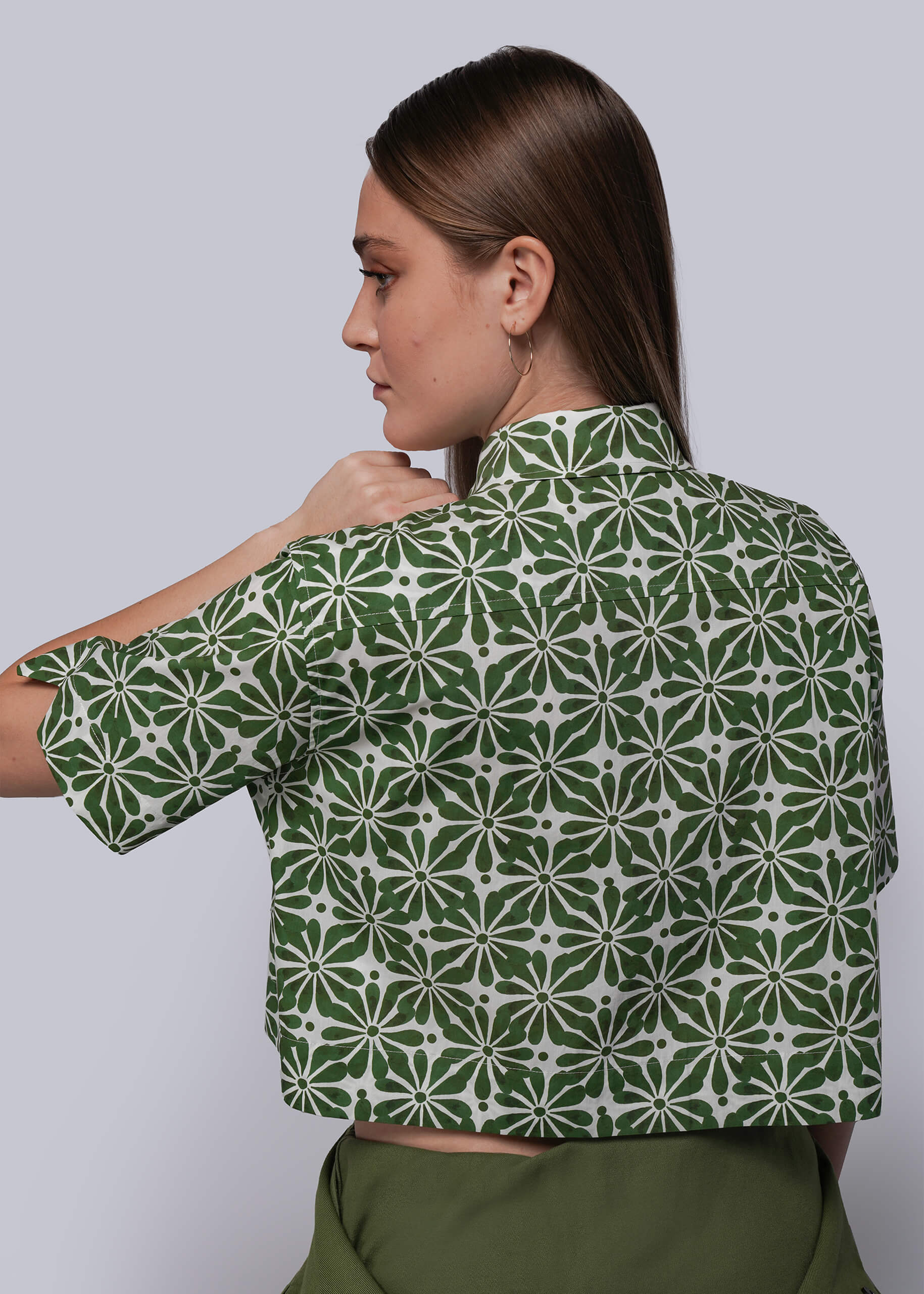 S=Woman wearing a green and white patterned blouse against a plain background