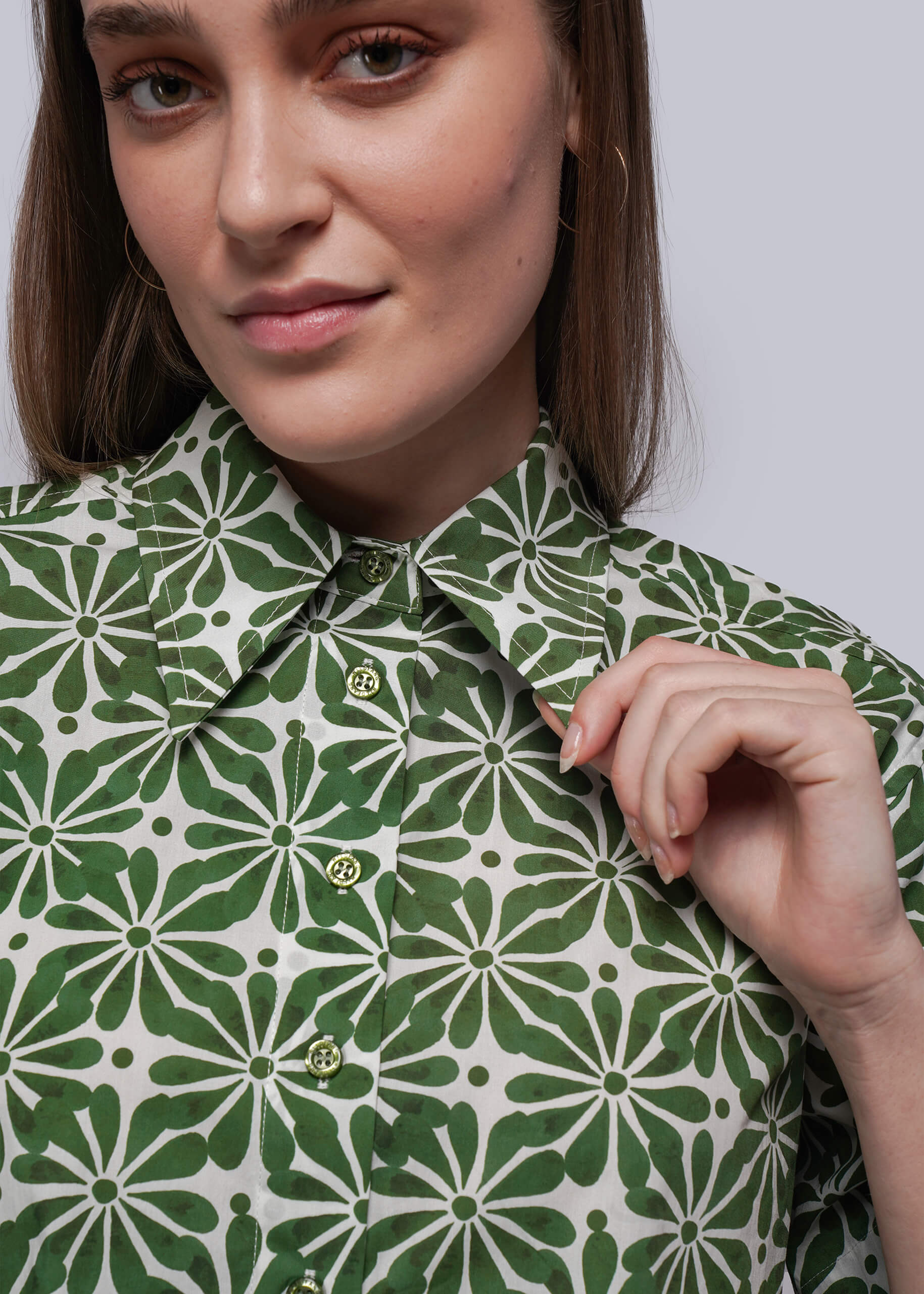 S=Woman wearing a green and white patterned shirt against a plain background