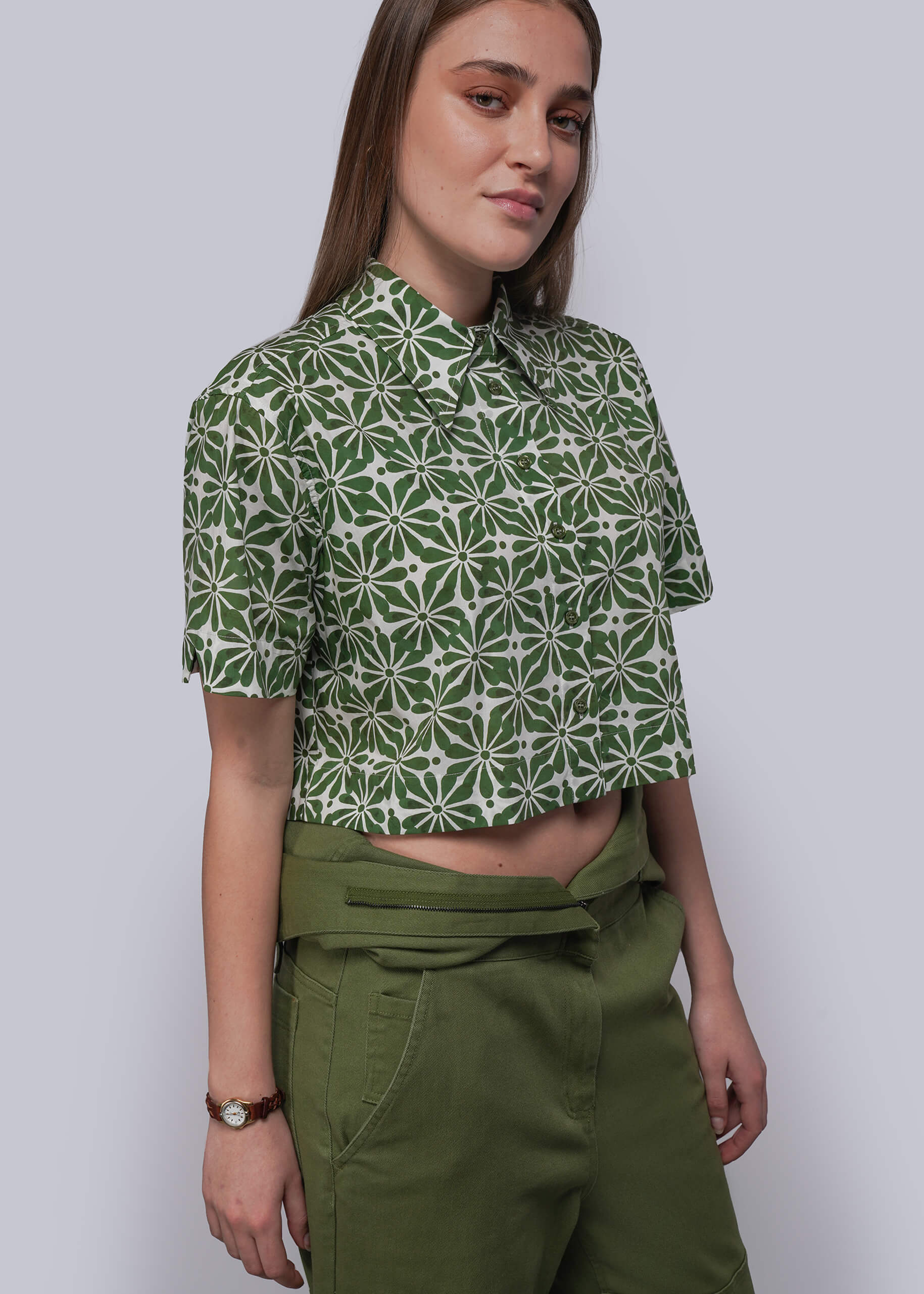 S=Woman wearing a green patterned shirt and green pants against a plain background
