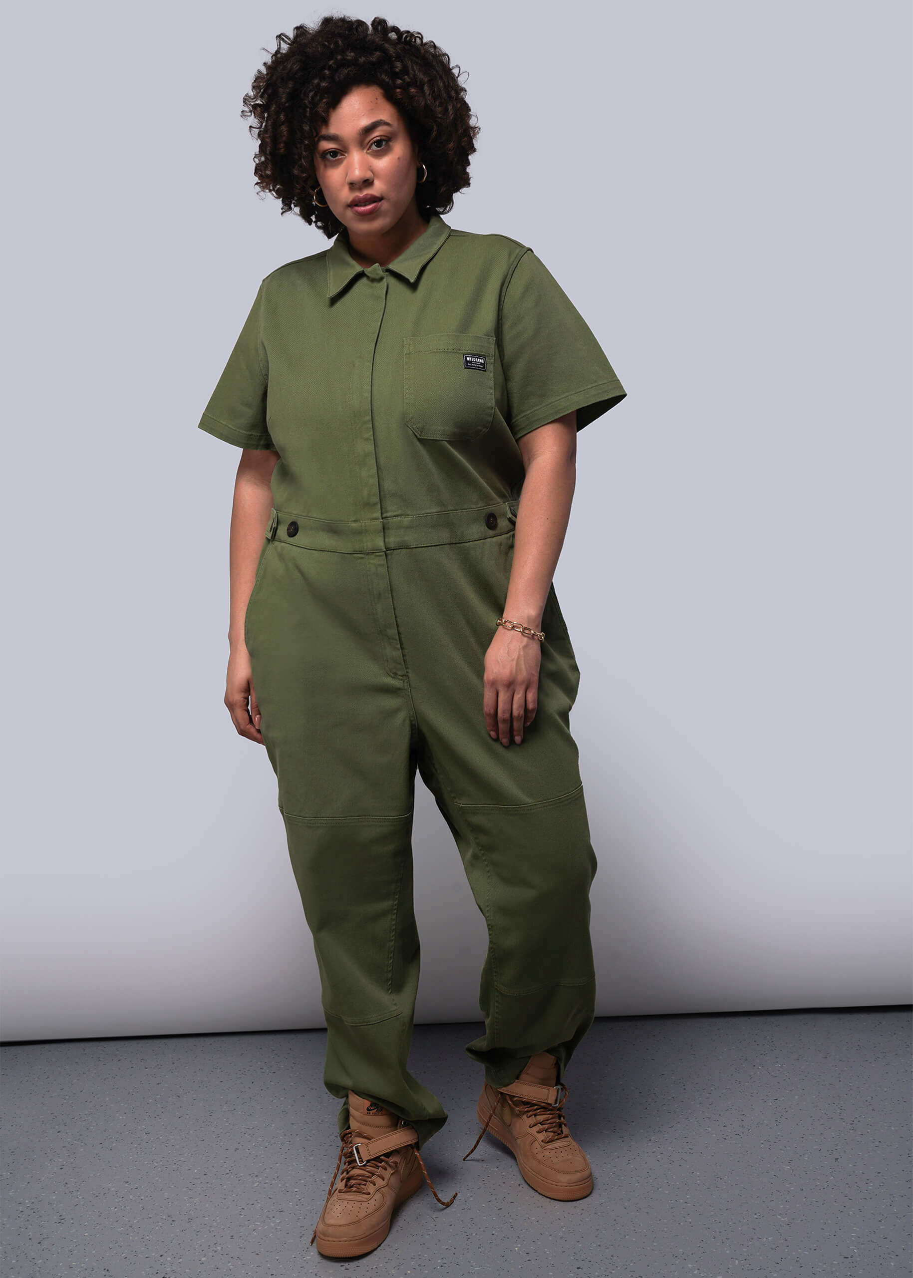 1X=Person wearing a green jumpsuit against a plain background