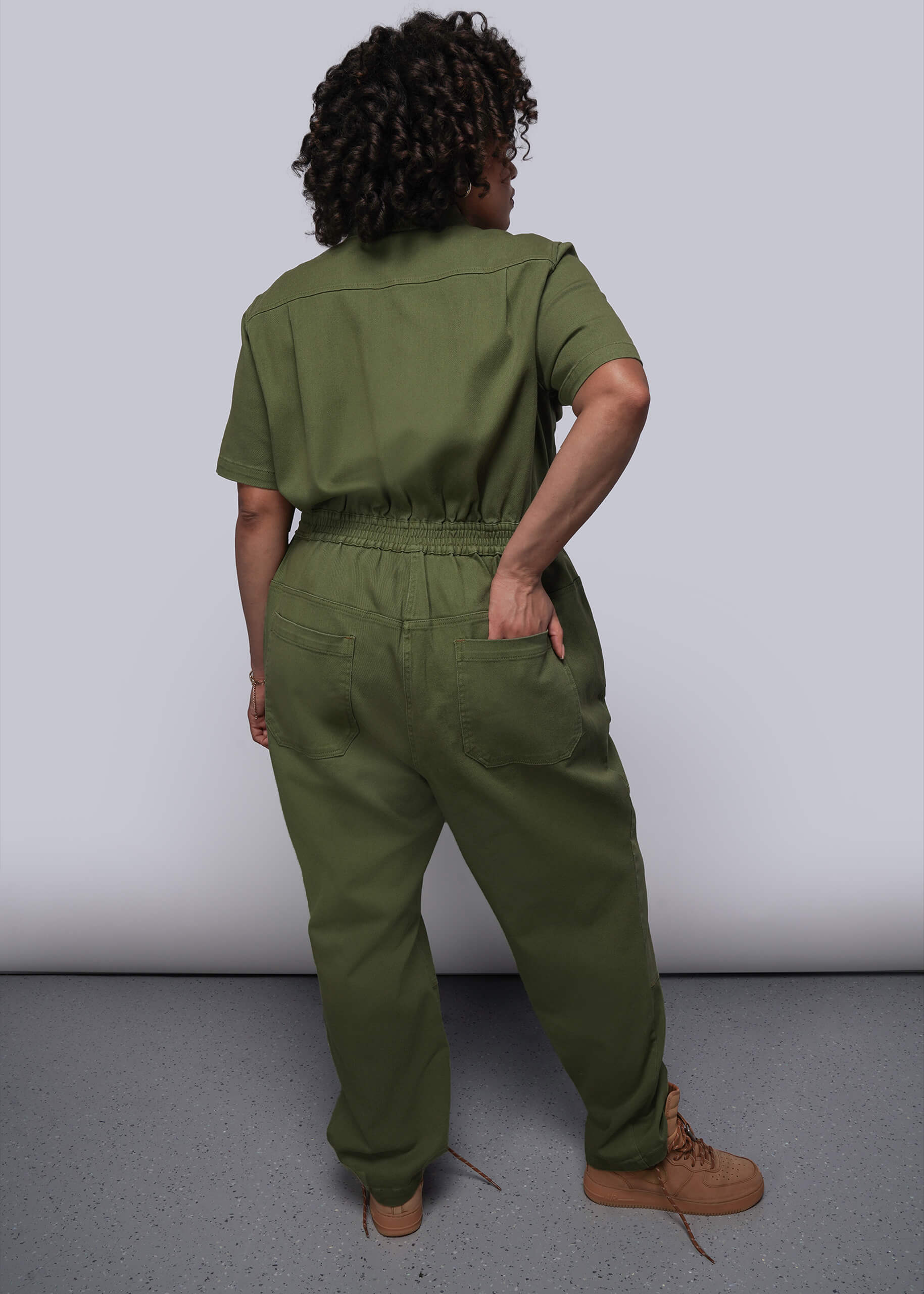 1X=Person wearing a green jumpsuit standing against a white background