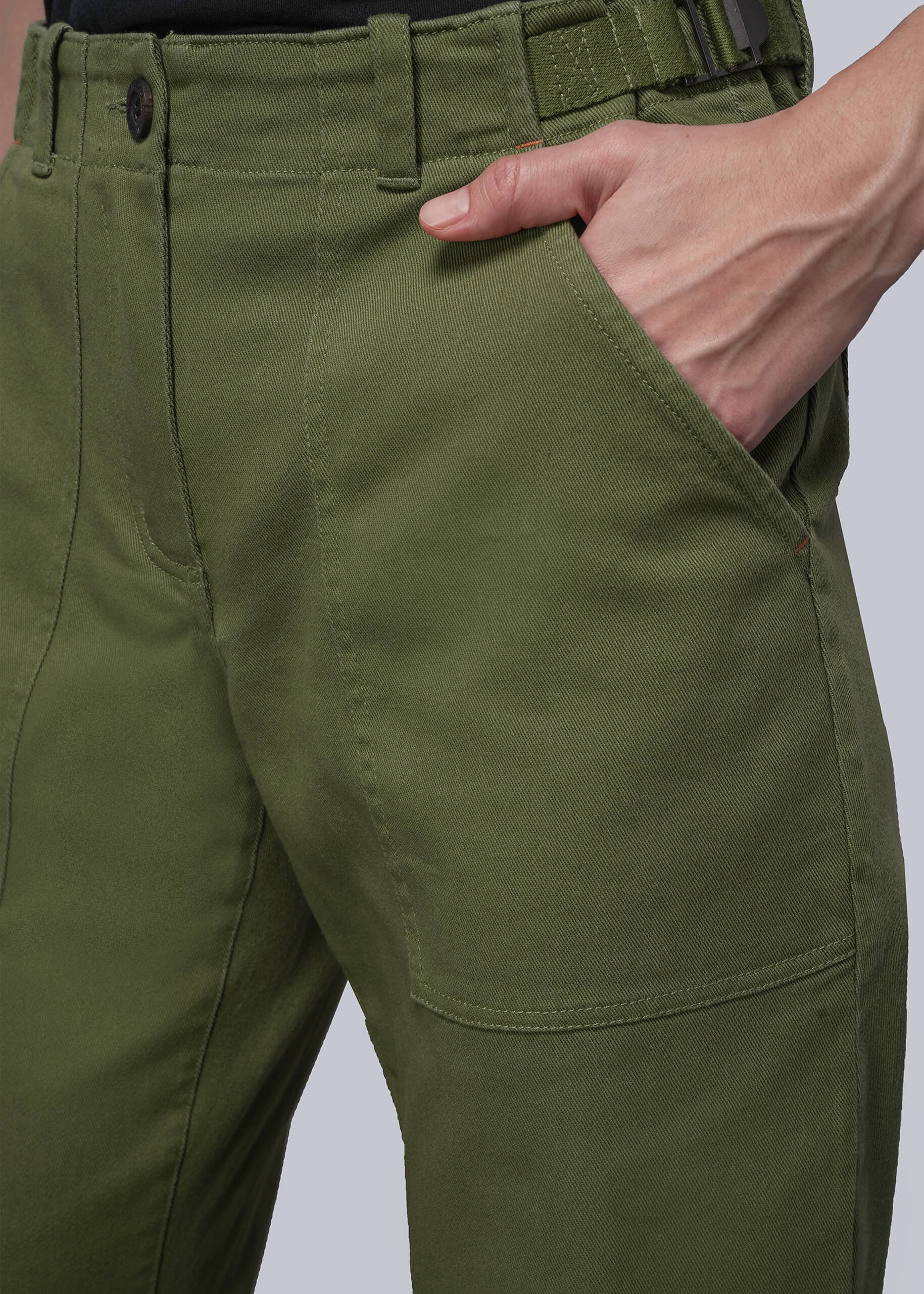 S=Close-up of green pants with a hand in the pocket on a light gray background