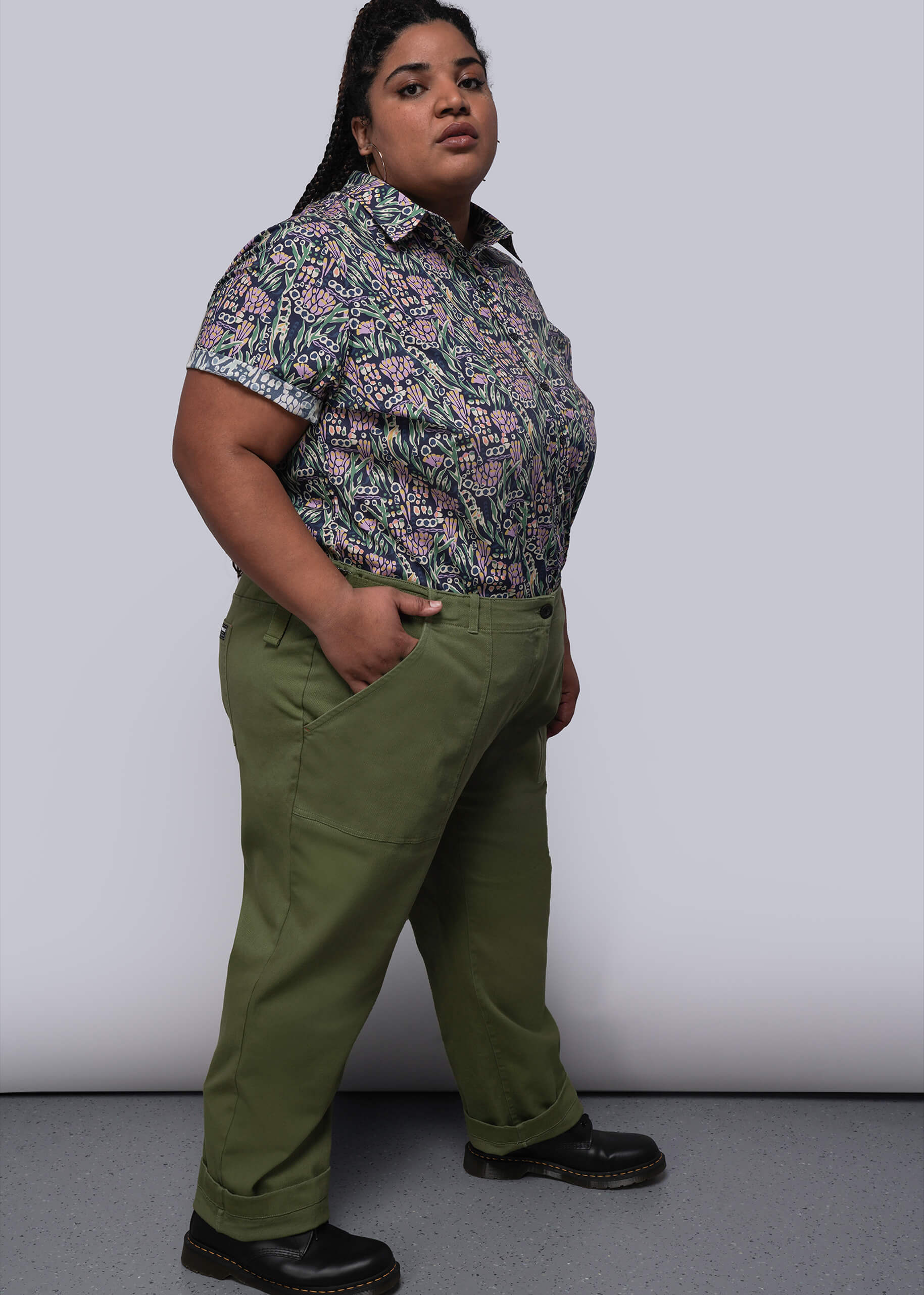 1X=Person wearing a patterned shirt and green pants against a plain background