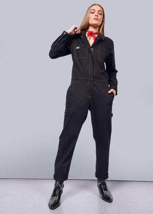 S=A person exudes confidence in The Essential Long Sleeve Coverall, crafted from brushed stretch cotton with an oversized fit and visible stitching, paired with black shiny shoes. A red patterned bandana graces their neck against the plain white background.