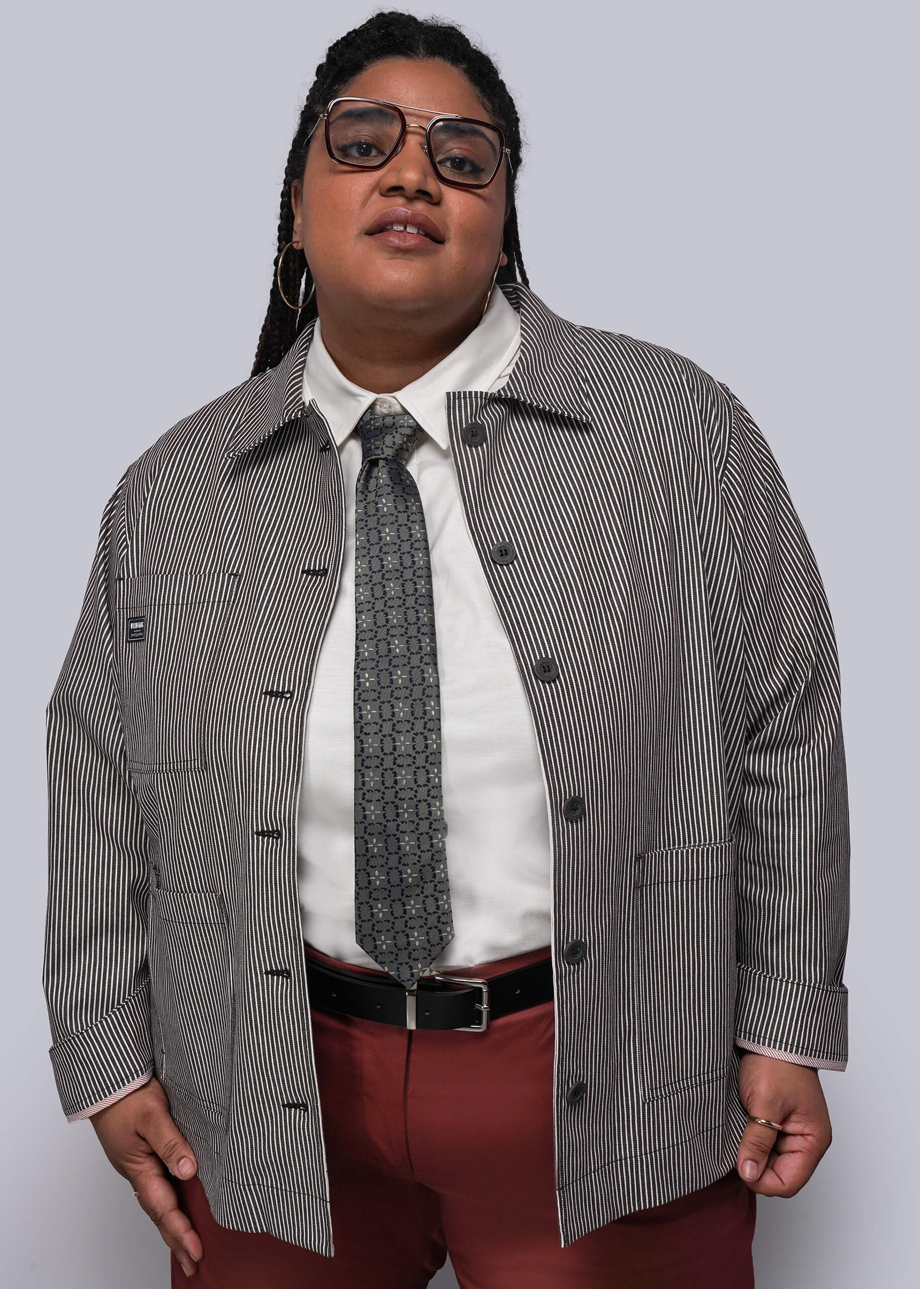 1X=Person wearing a brown and white striped jacket, white shirt, red pants, and patterned tie on a plain background