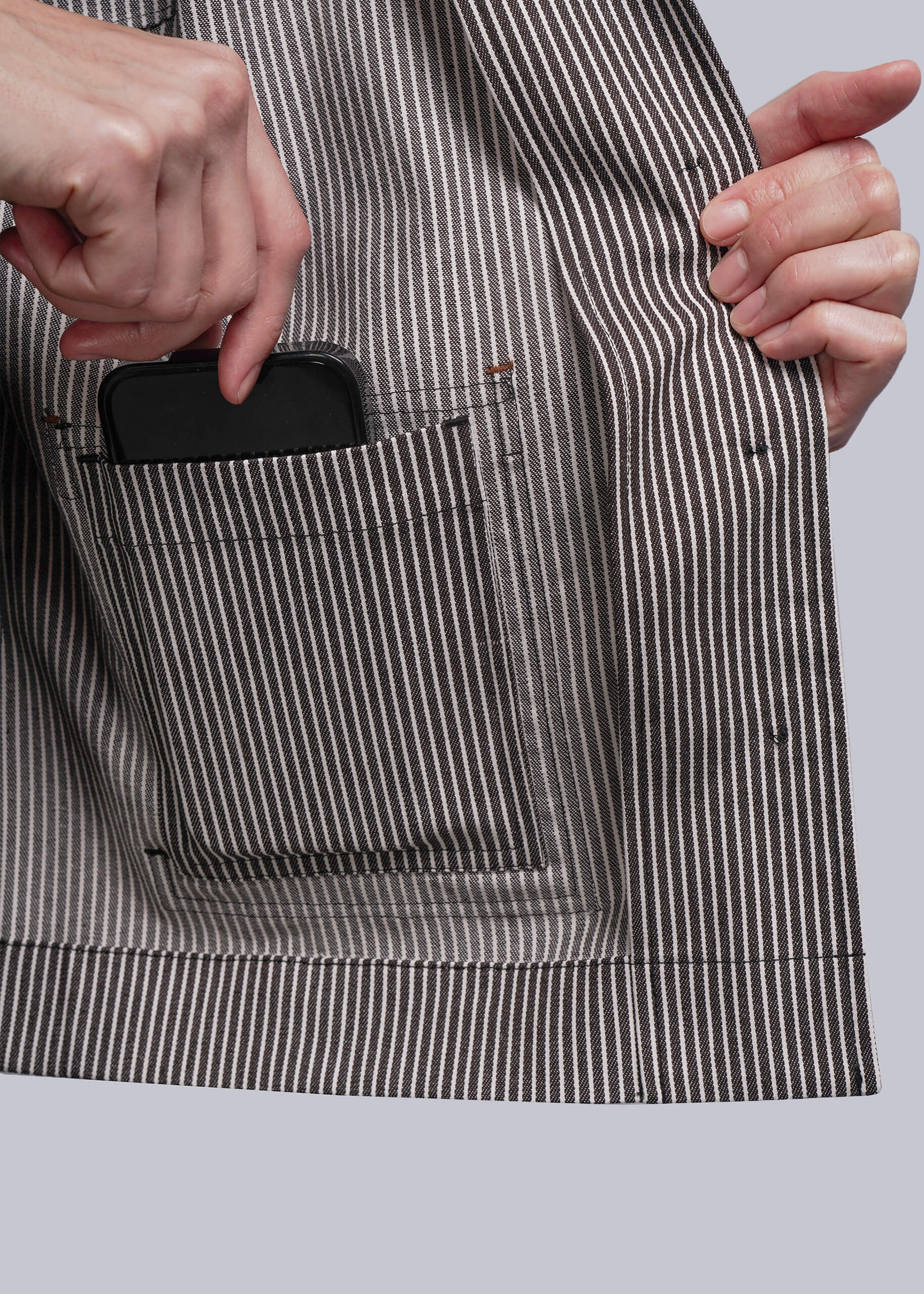 S=Person wearing a striped jacket with a phone in the pocket against a plain background