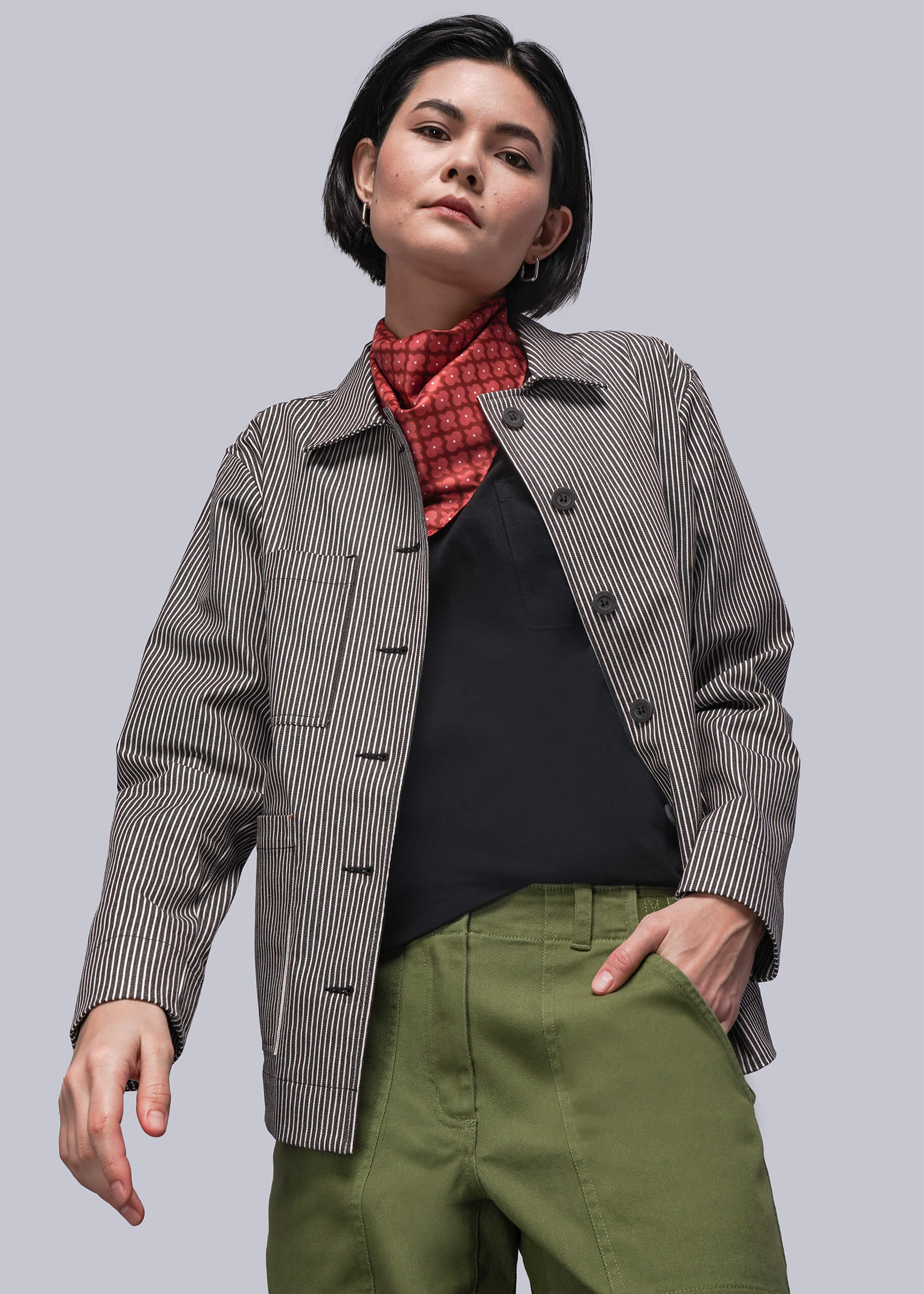 S=Person wearing a brown and white striped jacket, black shirt, and green pants on a light gray background