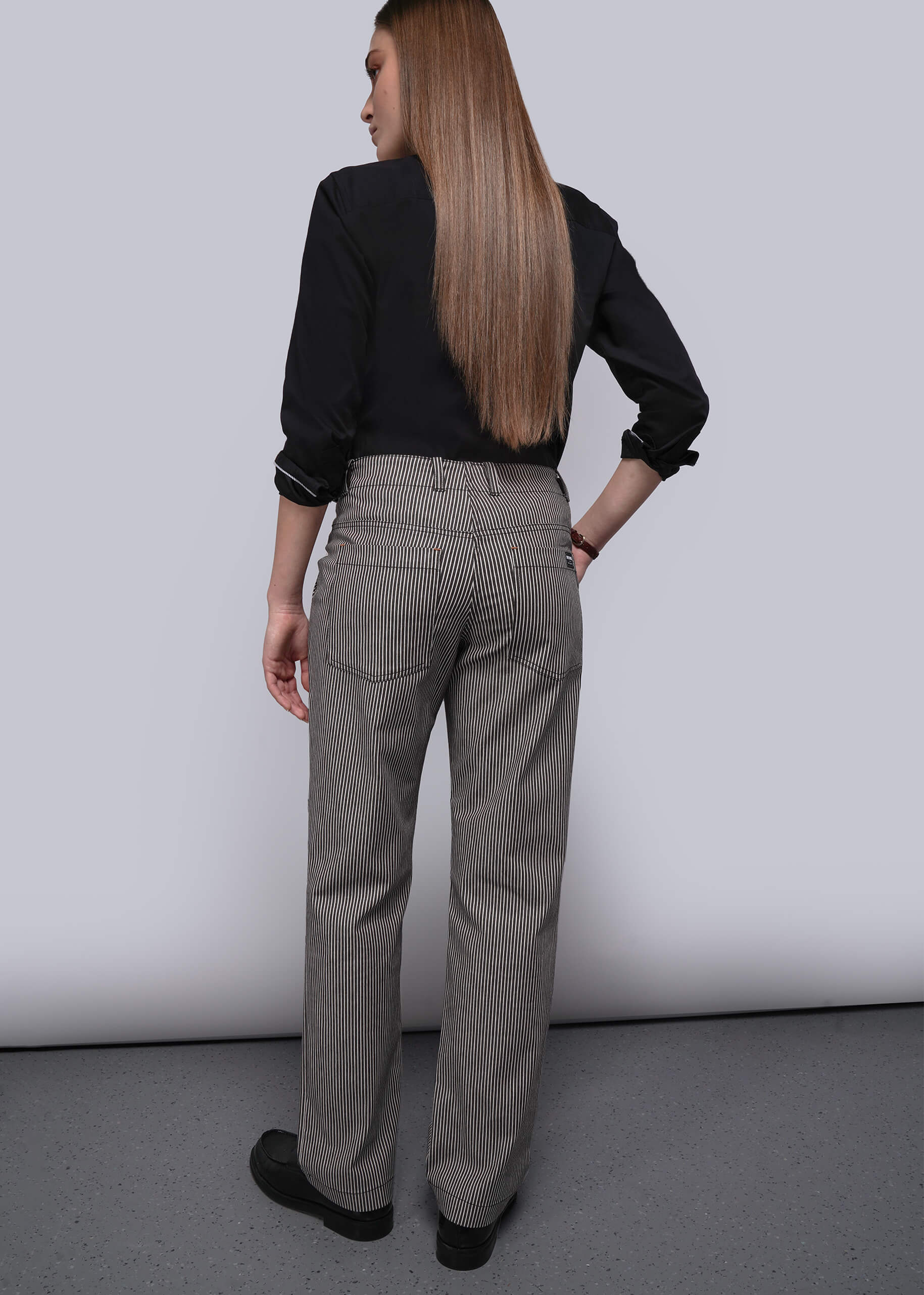 S=Person wearing a black shirt and brown and white striped pants against a plain background