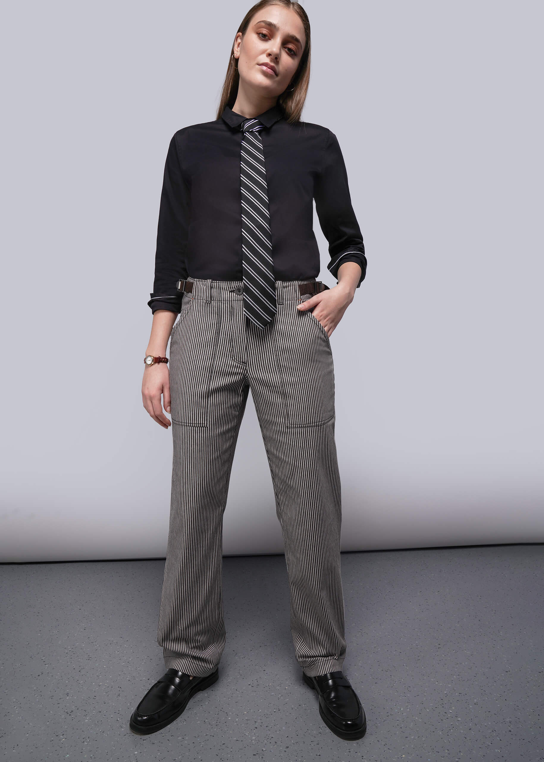 S=Person wearing a black shirt, gray tie, and brown and white striped pants against a plain background