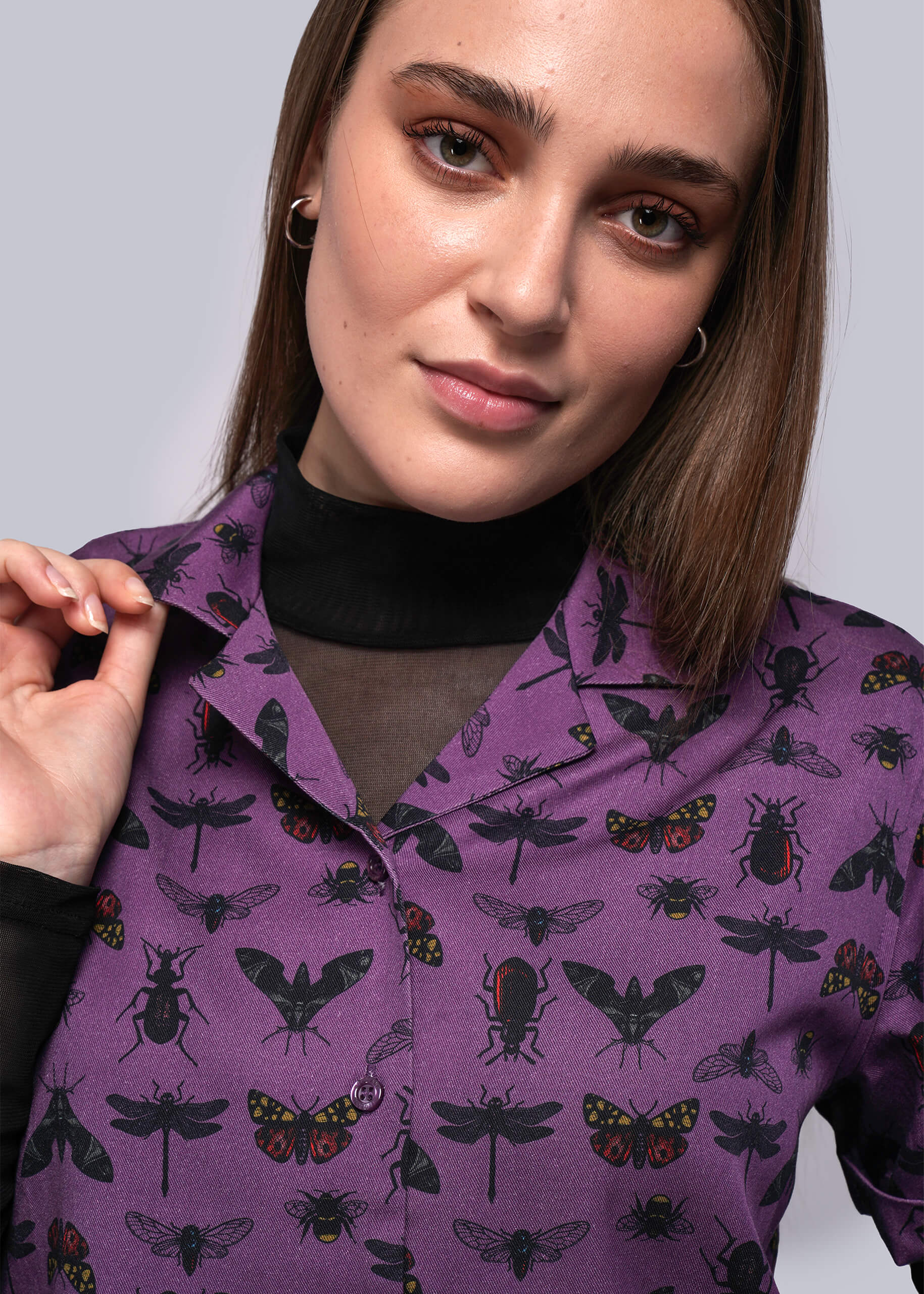 Woman wearing a purple shirt with insect pattern against a plain background