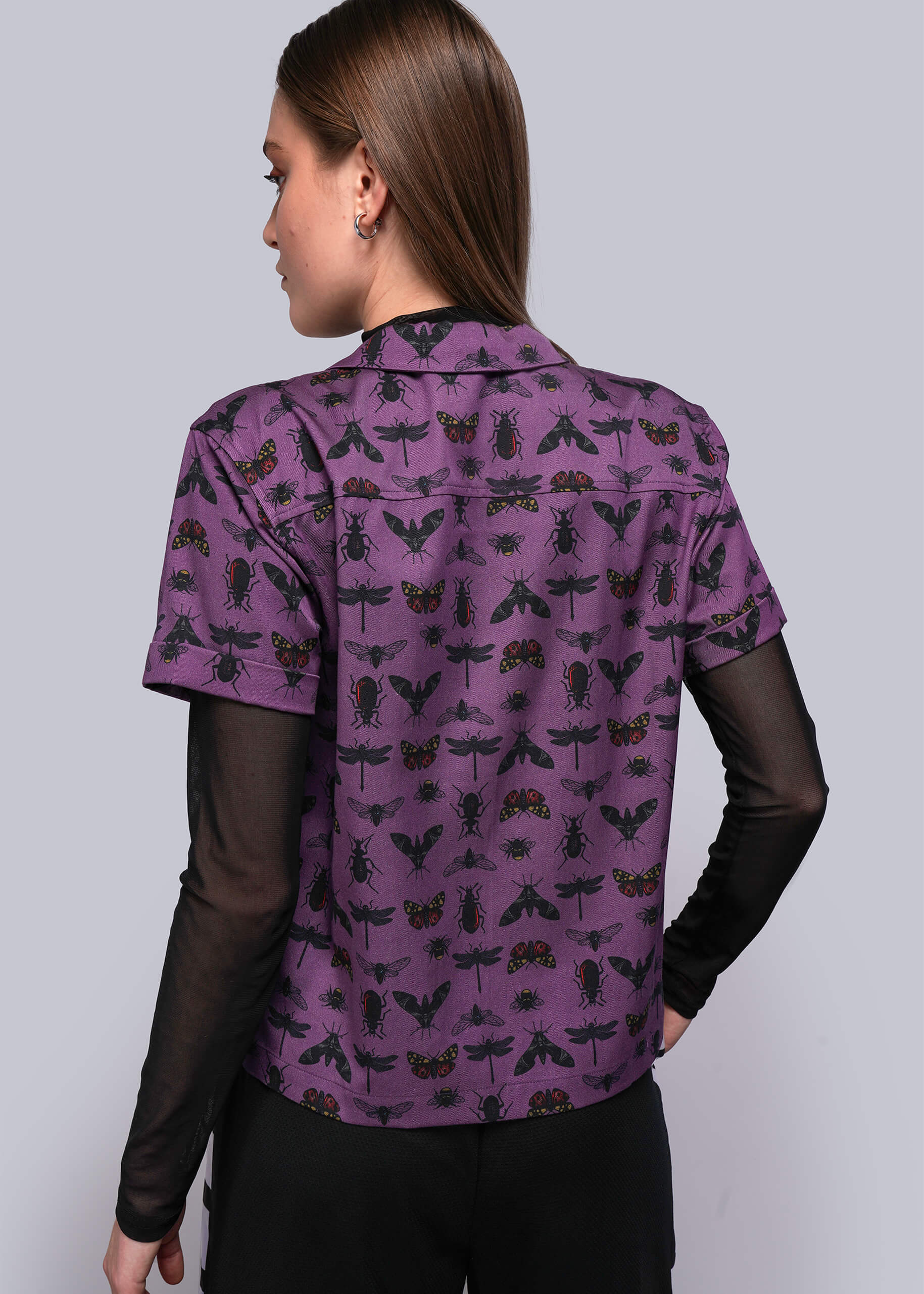 S=Woman wearing a purple shirt with insect pattern on a plain background
