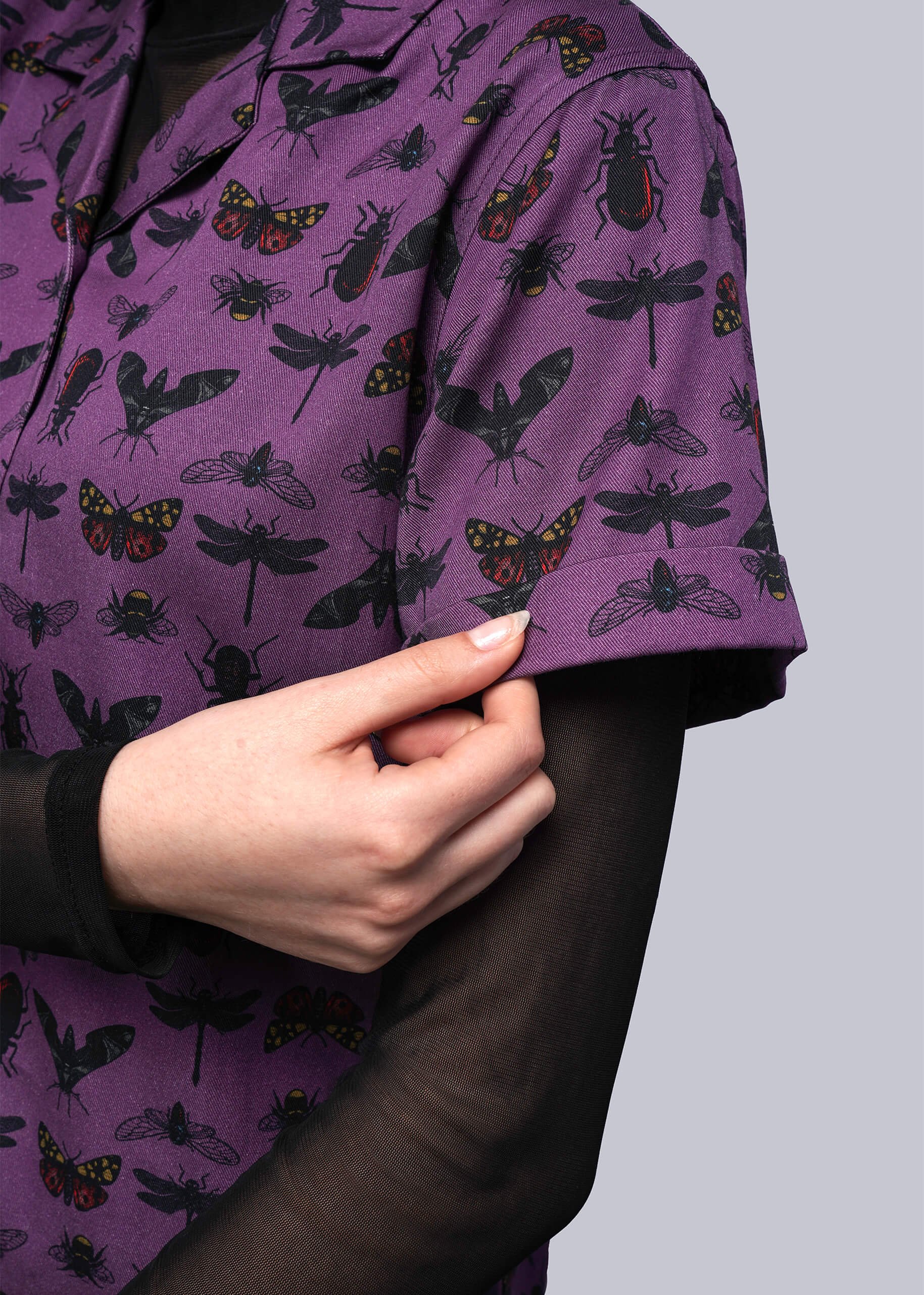S=Purple shirt with insect pattern worn by a person, with a hand adjusting the sleeve.