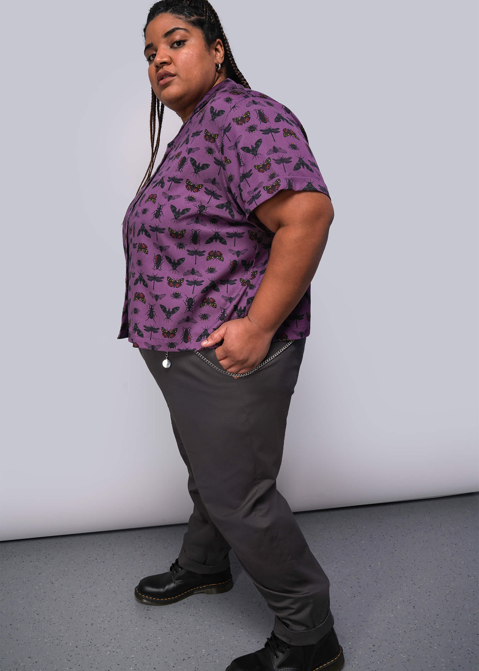 1X=Person wearing a purple patterned shirt and gray pants against a plain background