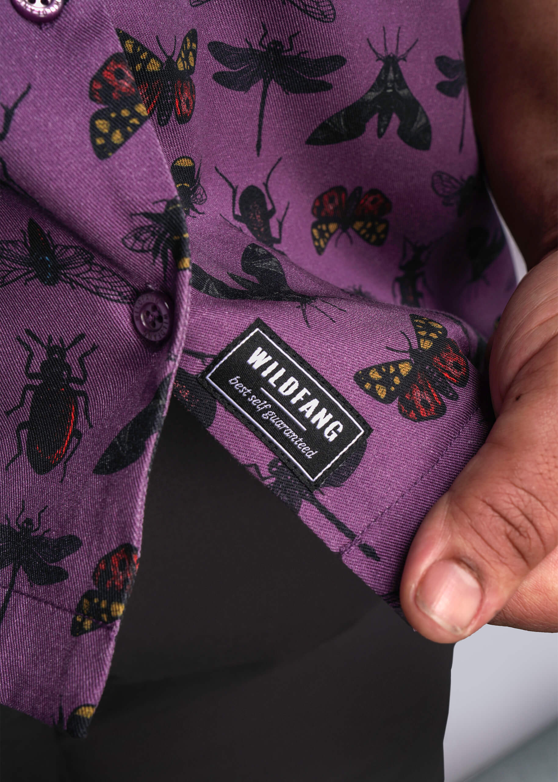 1X=Purple pocket square with insect pattern and Wildfang label held by a hand.
