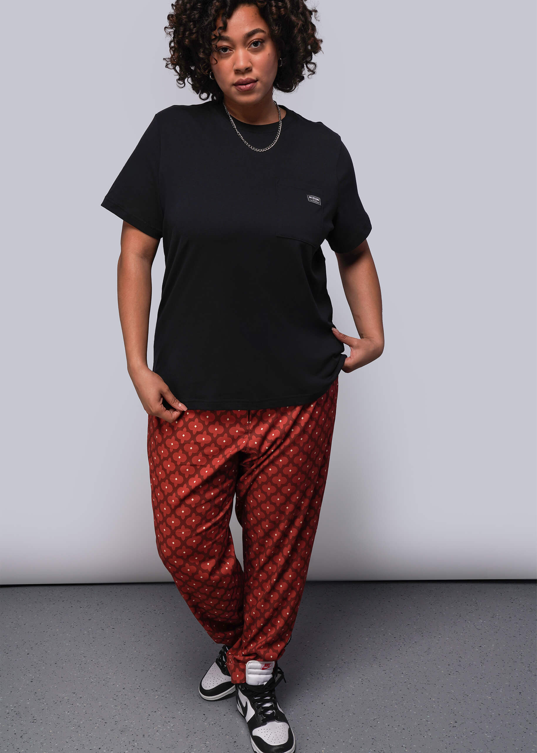 1X=Person wearing a black t-shirt and red patterned pants on a plain background
