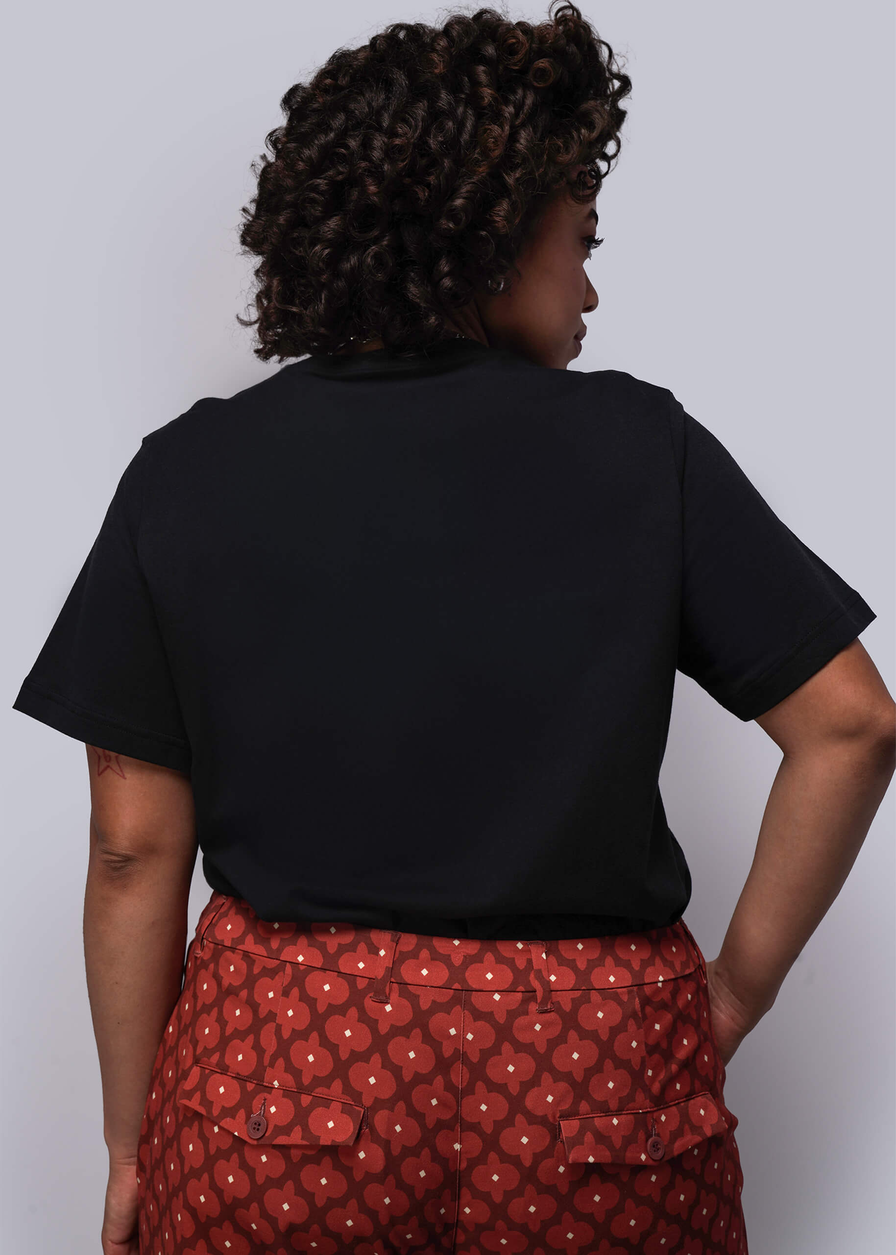 1X=Person wearing a black shirt and red patterned pants against a plain background