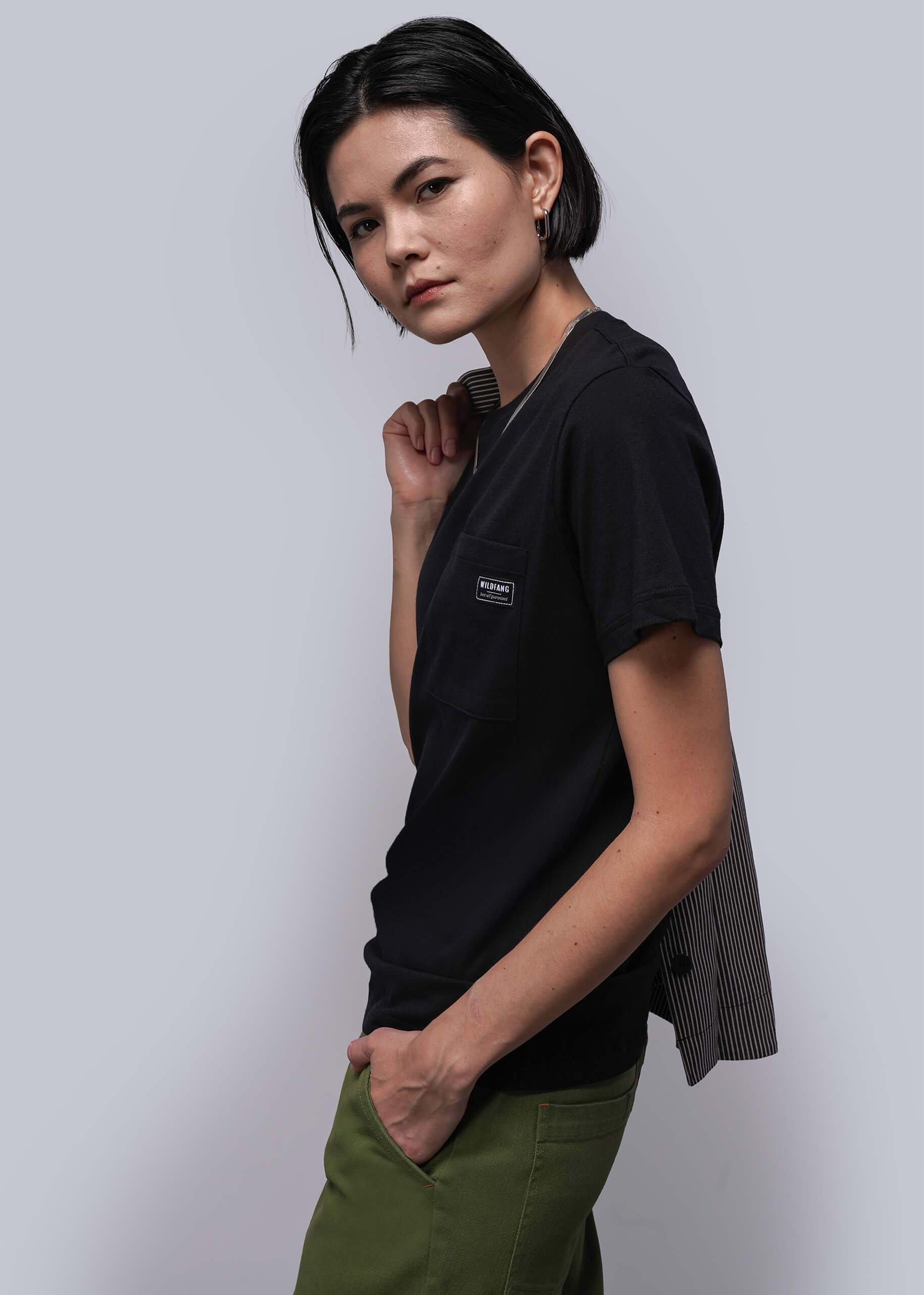 S=Woman wearing a black t-shirt with a logo and green pants against a white background