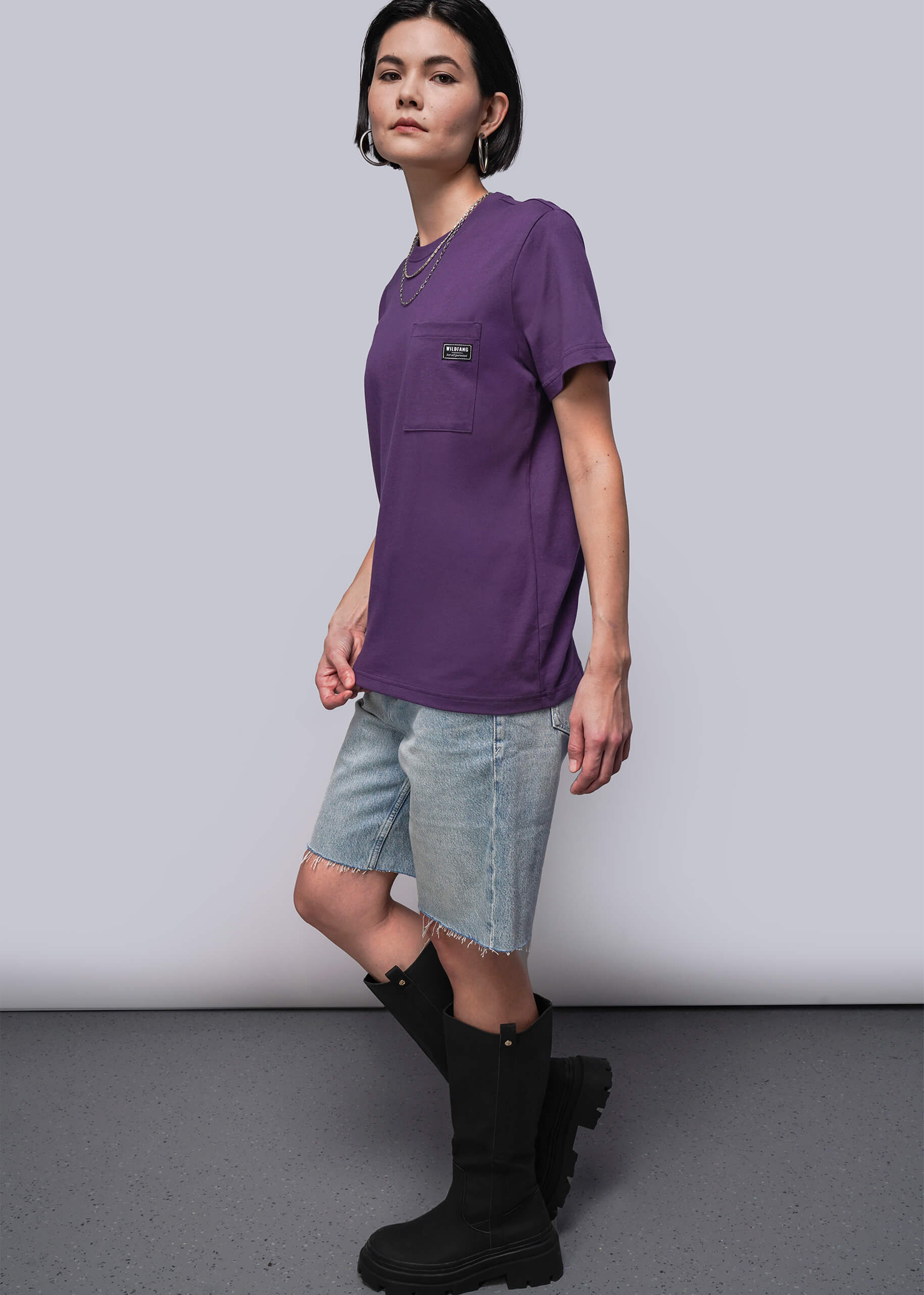 Person wearing a purple t-shirt, denim shorts, and black boots on a plain background