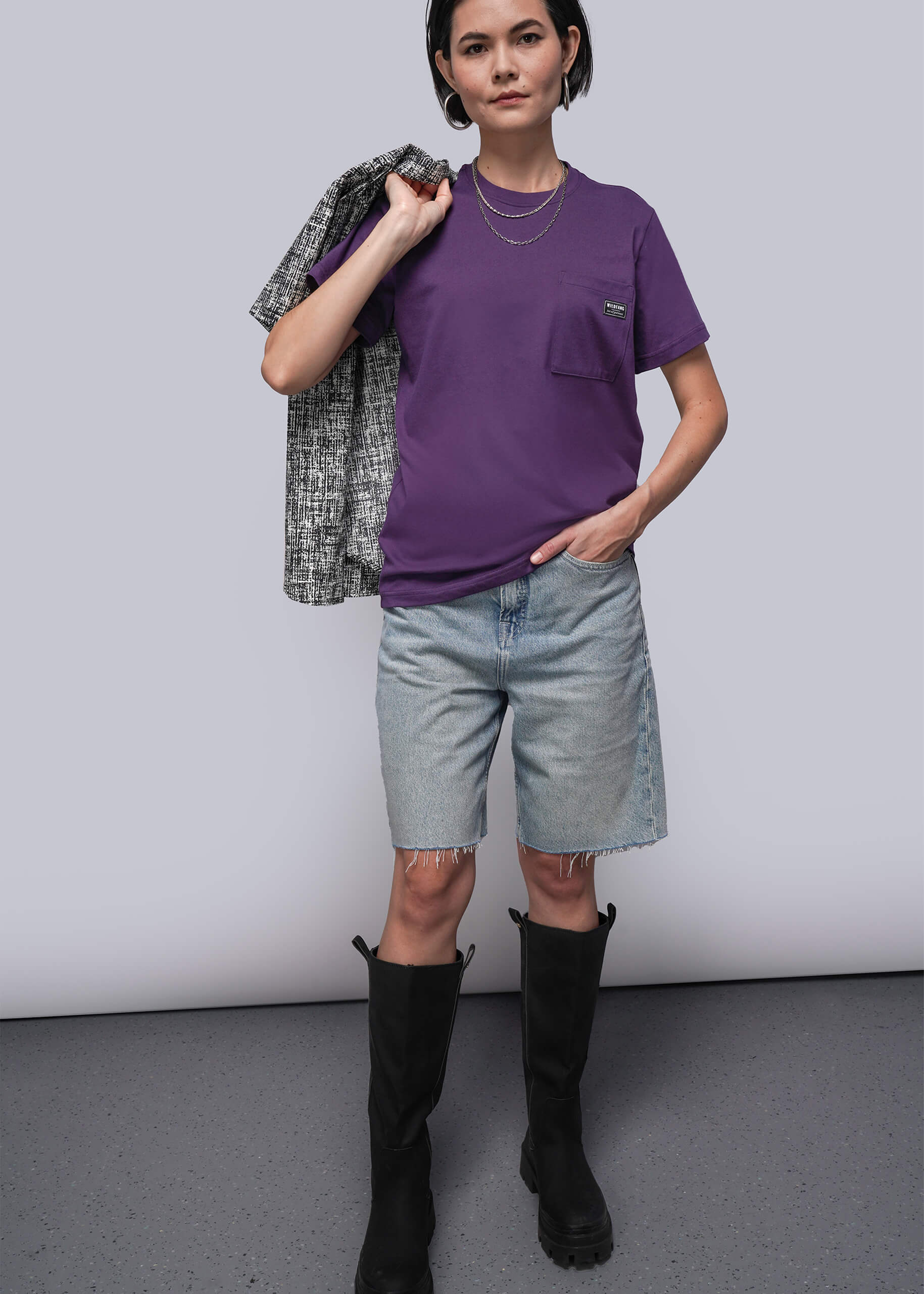 S=Person wearing a purple t-shirt, denim shorts, and black boots against a plain background