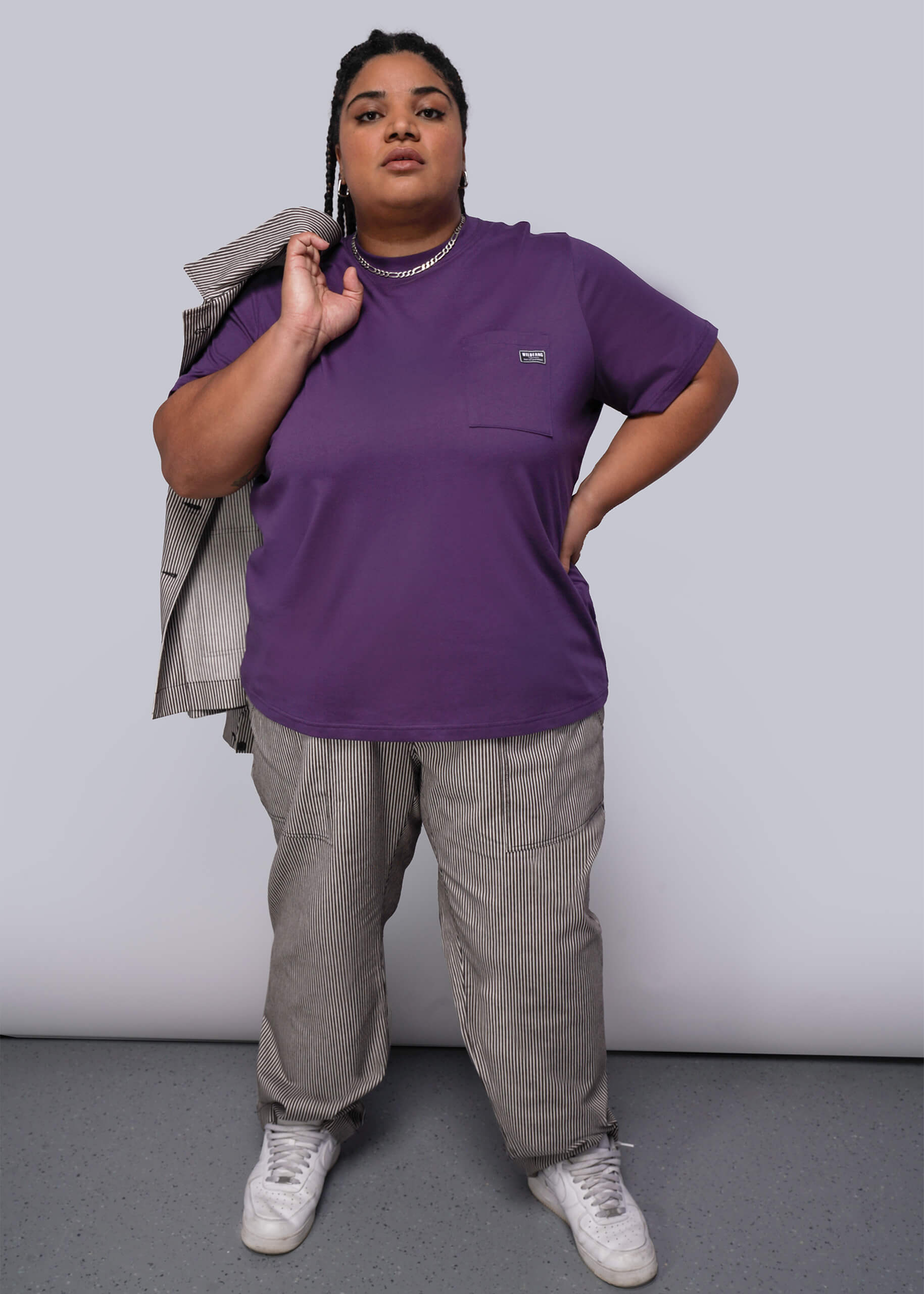1X=Person wearing a purple shirt and gray pants against a plain background