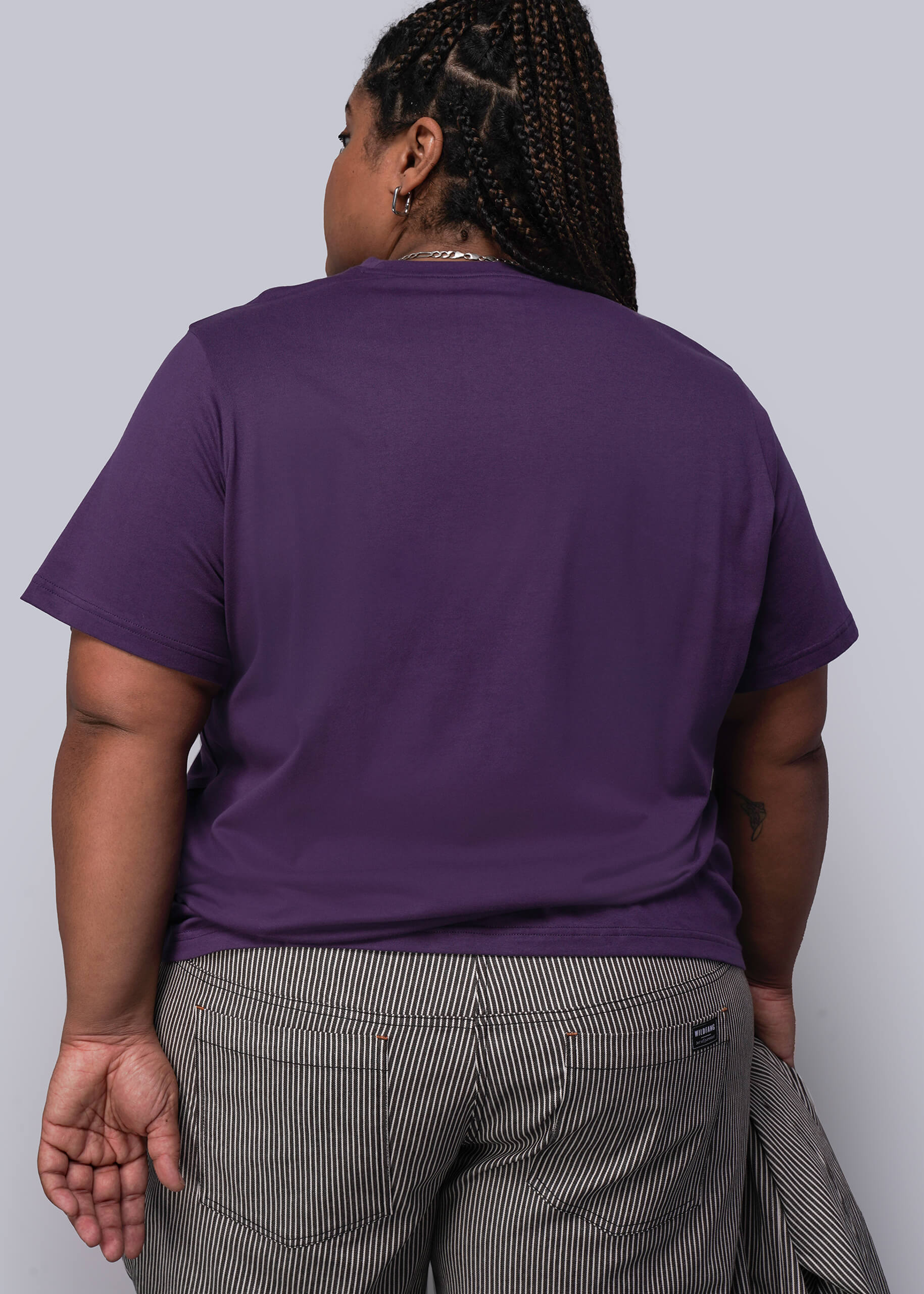 1X=Person wearing a purple t-shirt and gray pants against a light gray background