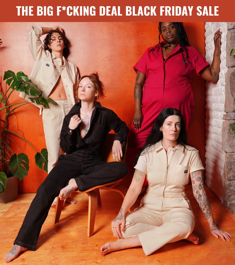 Group of people wearing Wildfang workwear styles pose in front of orange toned wood wall.