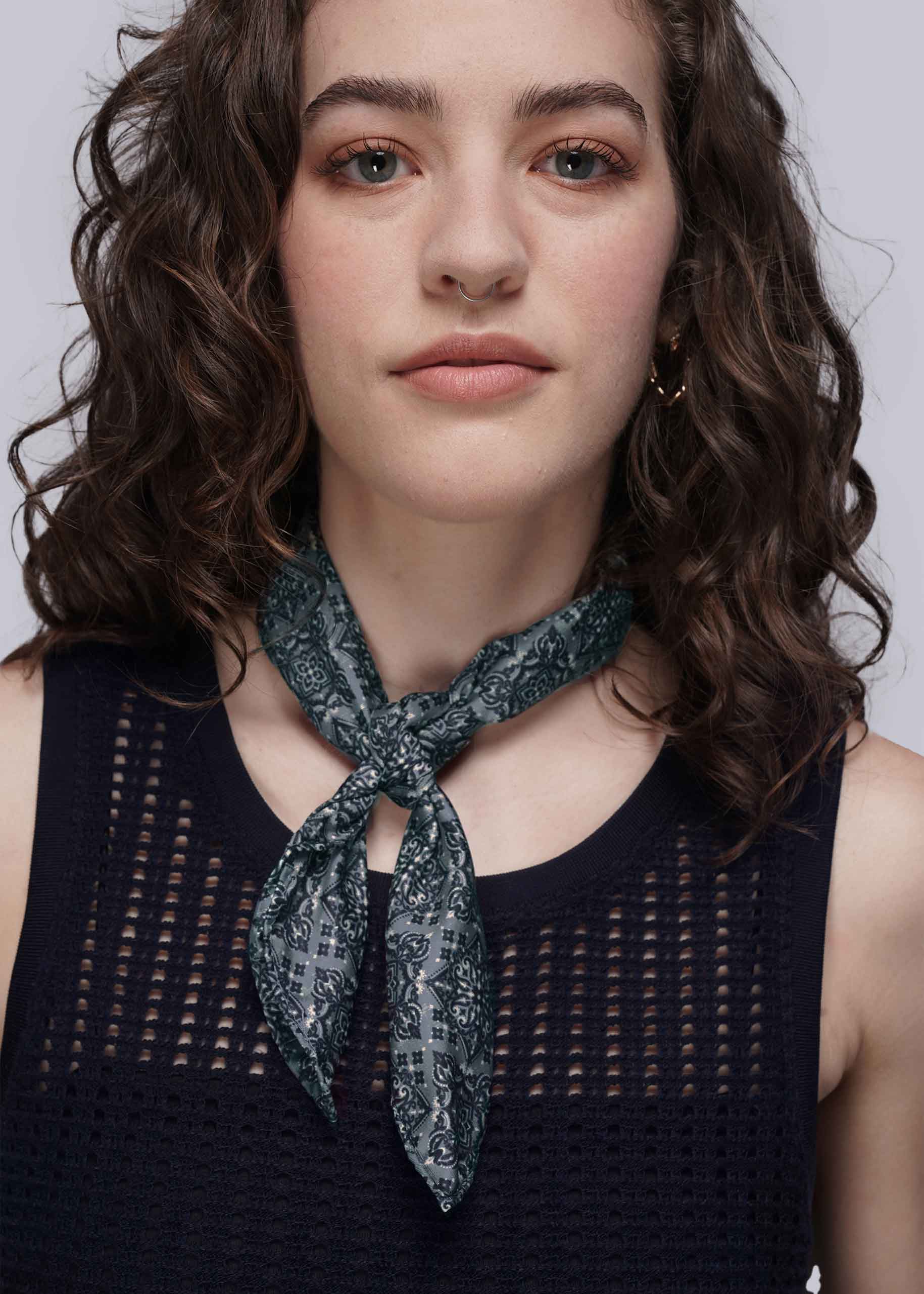 Woman wearing a teal patterned scarf around her neck against a plain background