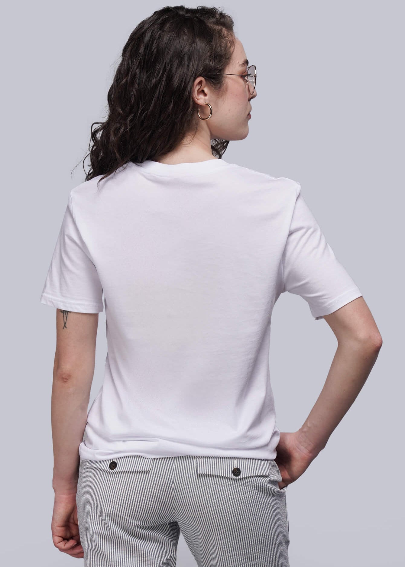 S=Back of person wearing a white t-shirt and gray pants on a plain background