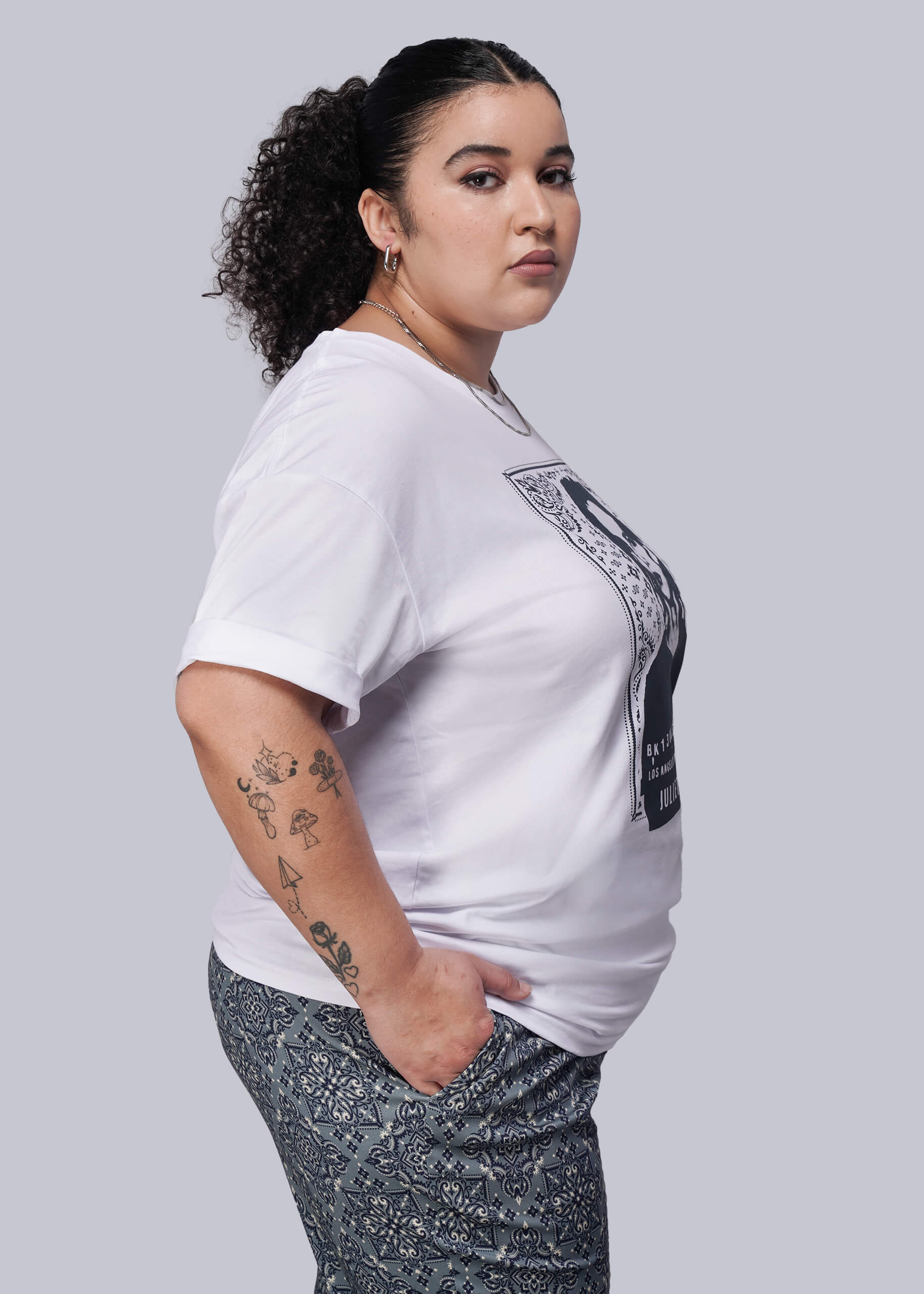 1X=Woman wearing a white t-shirt with a navy blue graphic design on a gray background